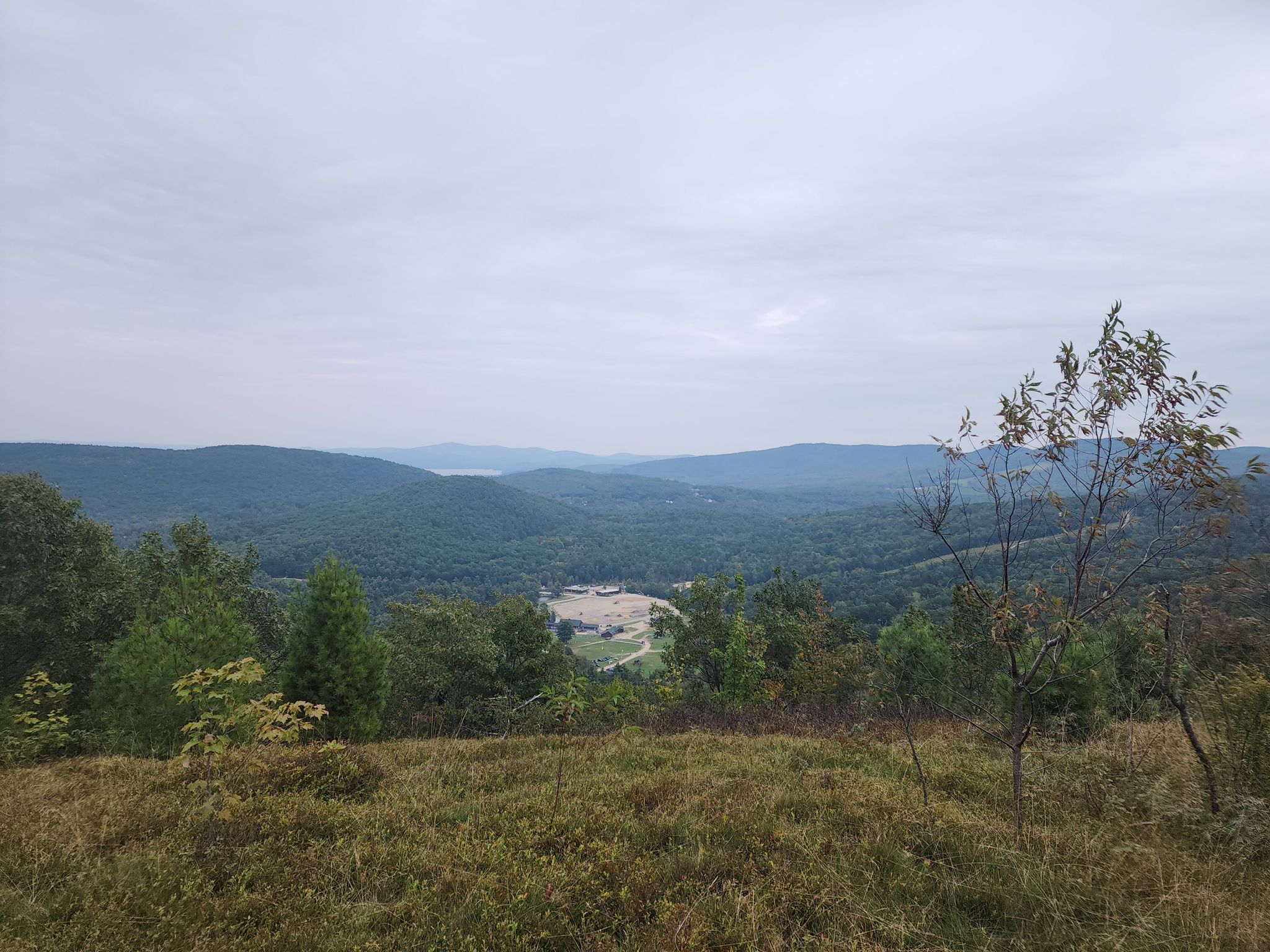 Overcast view of green forested mountains and a valley from a grassy hilltop. - Mt. Rowe Trail