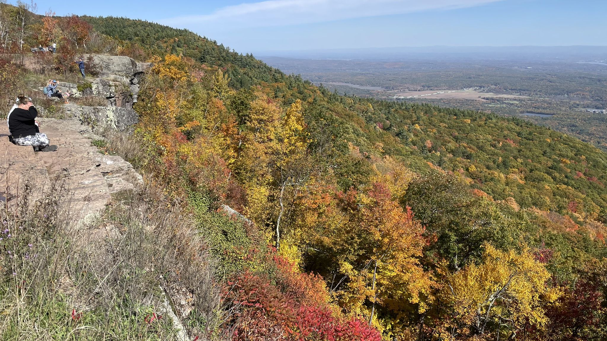 A person sits on a cliff overlooking an autumn forest and distant valley. - Inspiration Point via South Lake Road