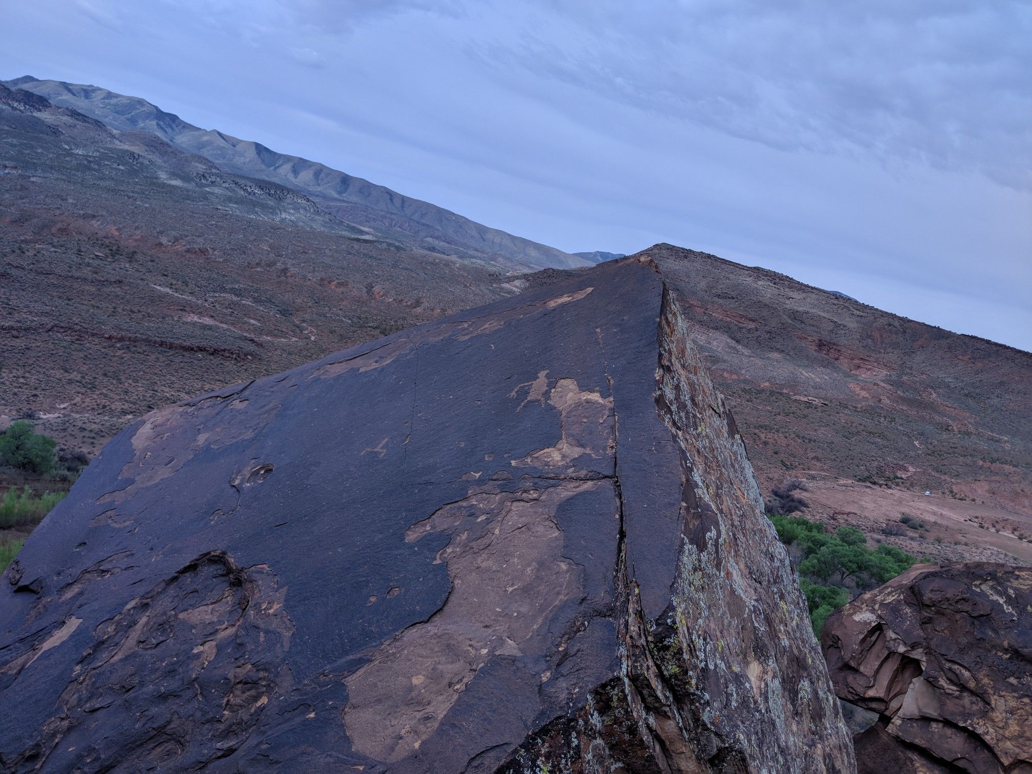 Dark rock with petroglyphs in foreground, arid mountains under cloudy sky. - Tempi'po'op Trail