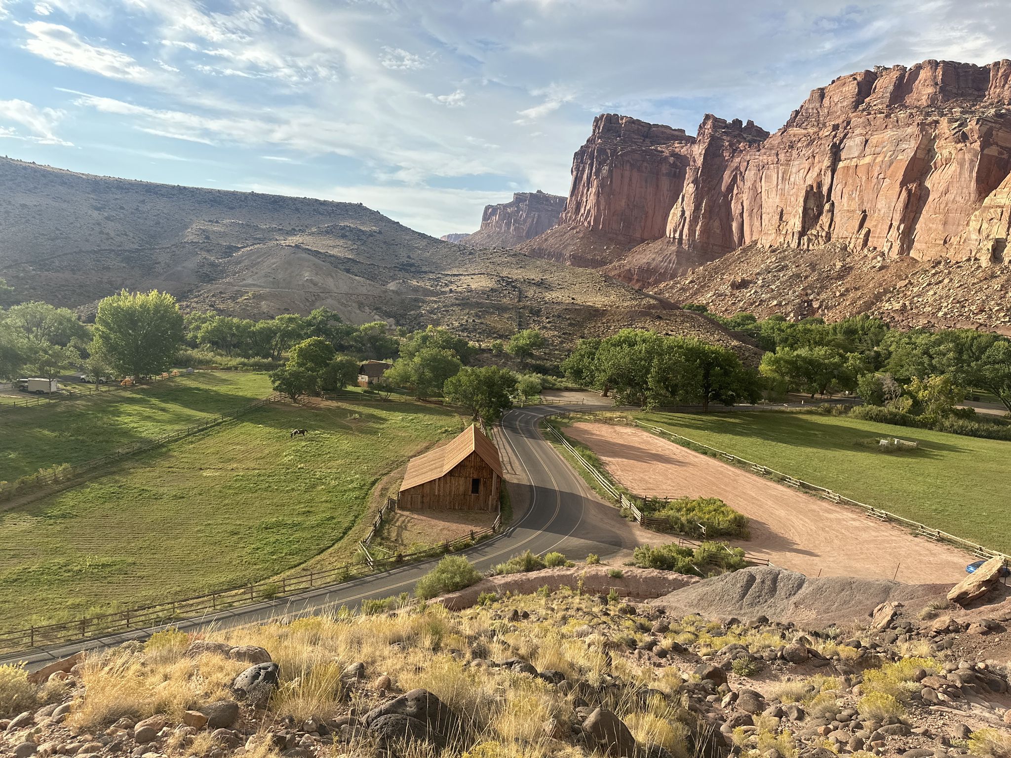 A wooden barn sits in a green valley beneath towering red cliffs. - Cohab Canyon Trail – South Fruita Overlook loop from Fruita