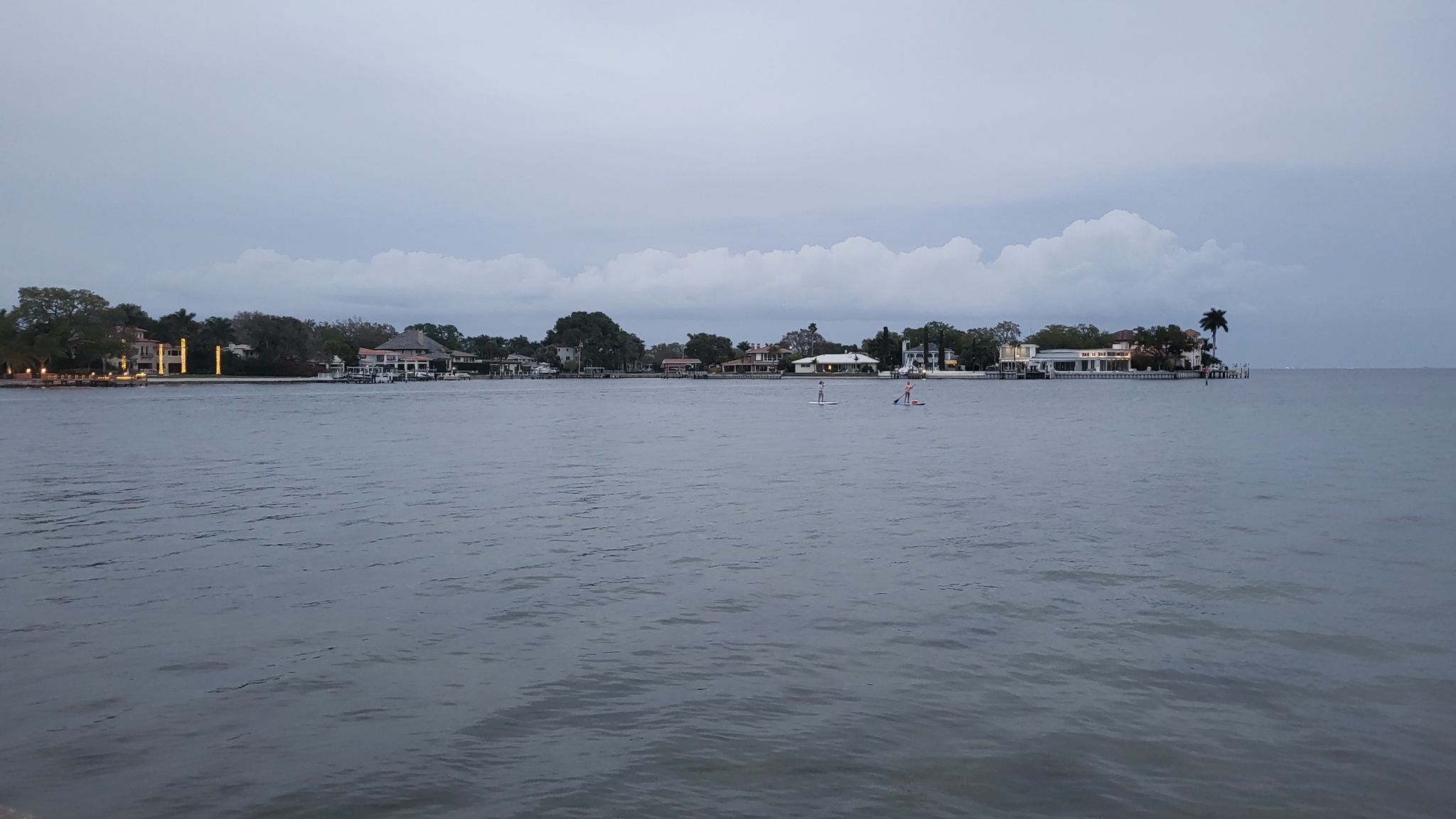 Wide body of water with distant houses under an overcast, cloudy sky. - View of St. Pete Pier – Beach at North Shore Park loop from Saint Petersburg