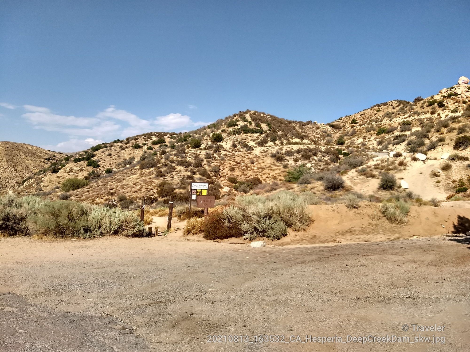 A dirt parking area at the base of arid hills with a wooden sign. - Mojave Forks River Dam Overlook Trail