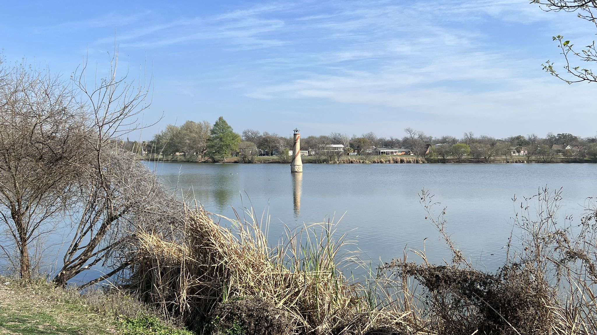 Bright daylight on a calm lake with a tall structure and dry reeds in foreground. - Apache and Alazan Creek Greenway Trail