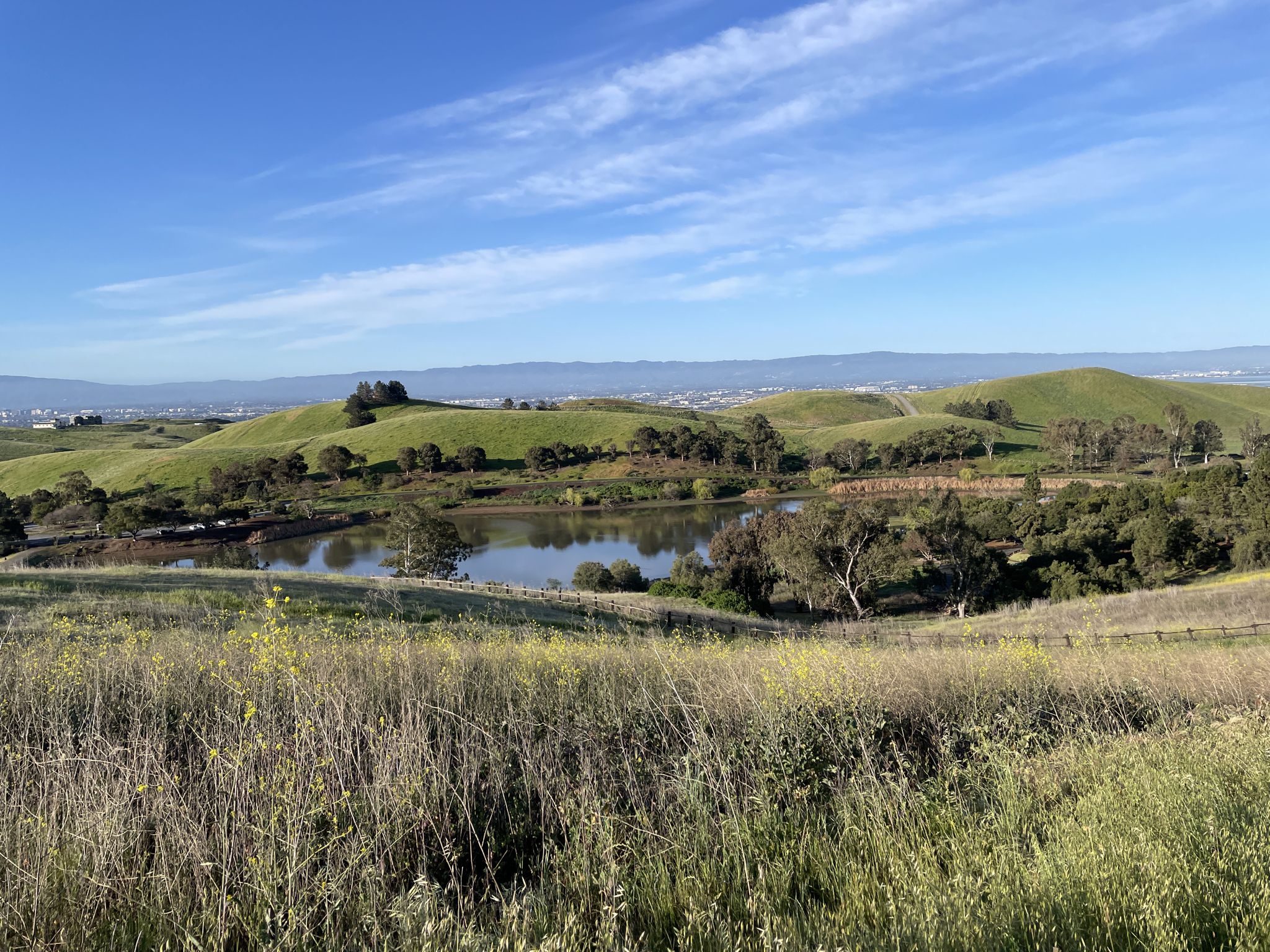 Sunny landscape with green rolling hills, a calm lake, and blue sky. - Monument Peak Trail