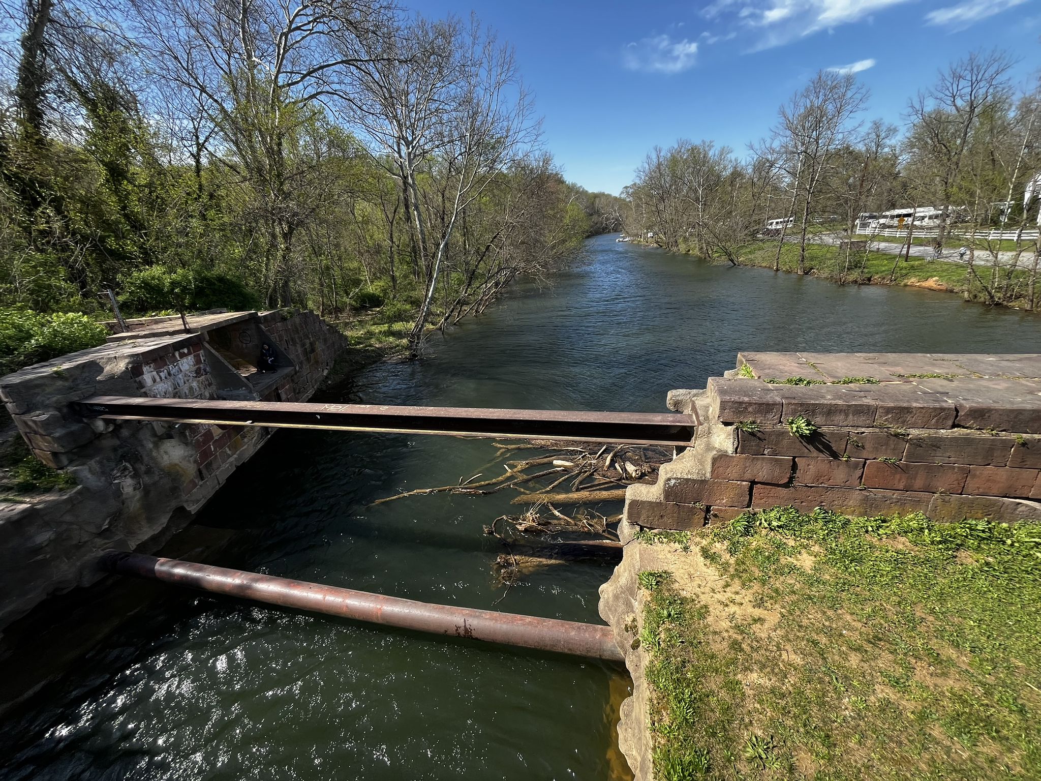 River flowing under a stone bridge with metal beams, surrounded by trees. - Chesapeake and Ohio Canal Towpath