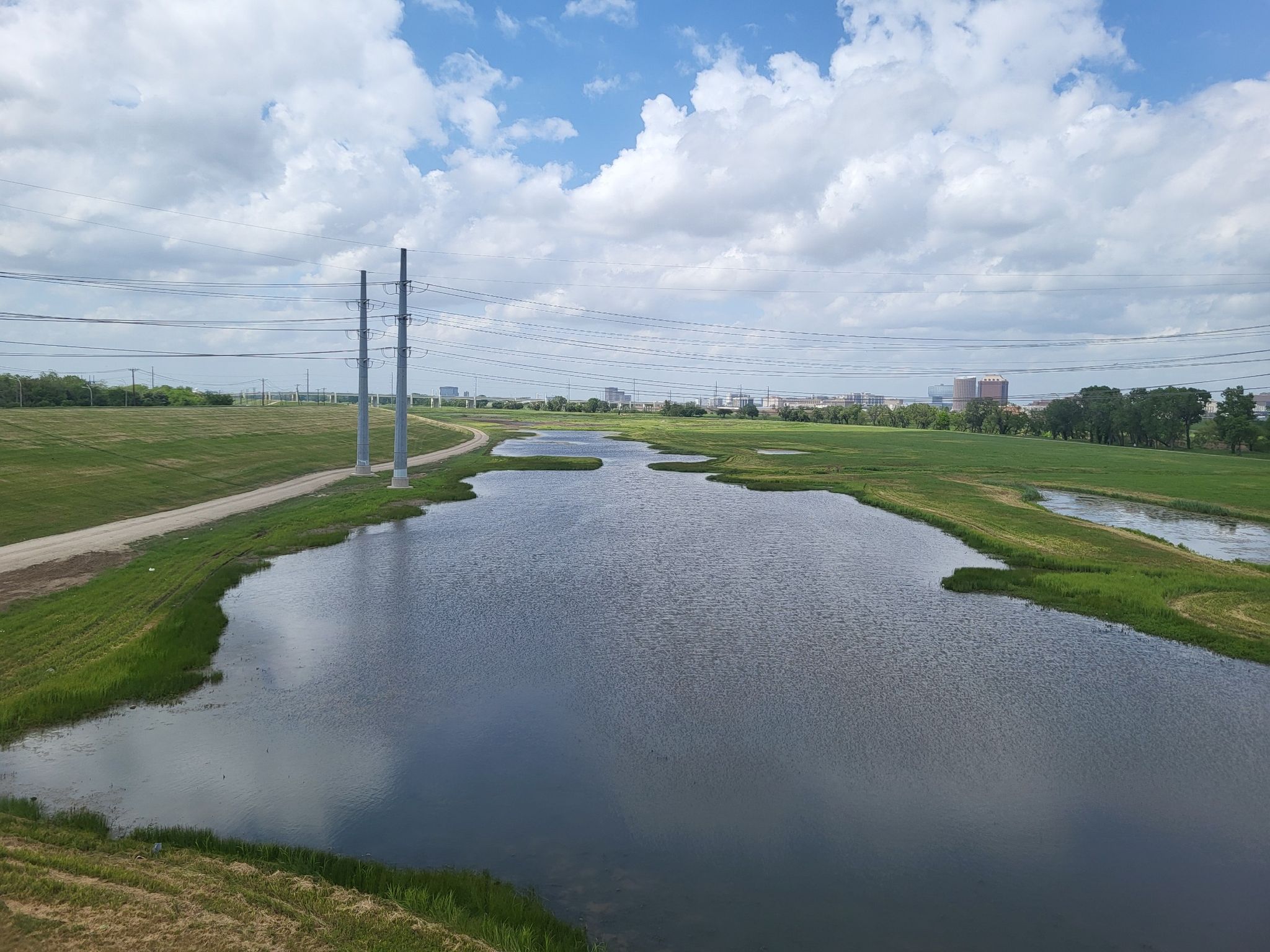 Wide river surrounded by green grassy banks under a cloudy sky. - Margaret Hunt Hill Bridge – Katy Trail loop from North Dallas High School