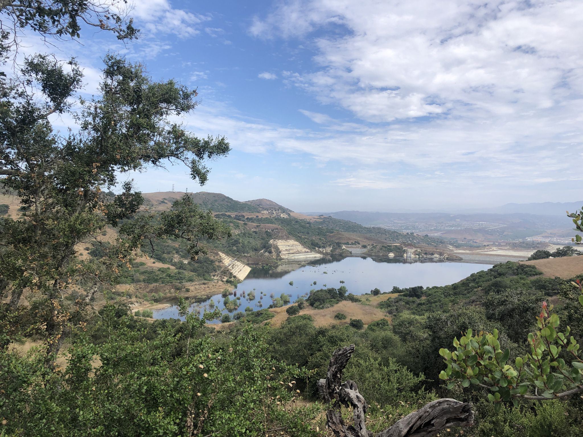 A scenic view of a lake nestled among green hills under a partly cloudy sky. - Talega Loop