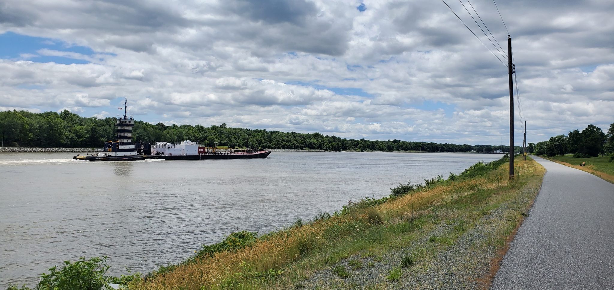 A tugboat pushes a barge on a wide river under cloudy skies. - C&D Canal Trail