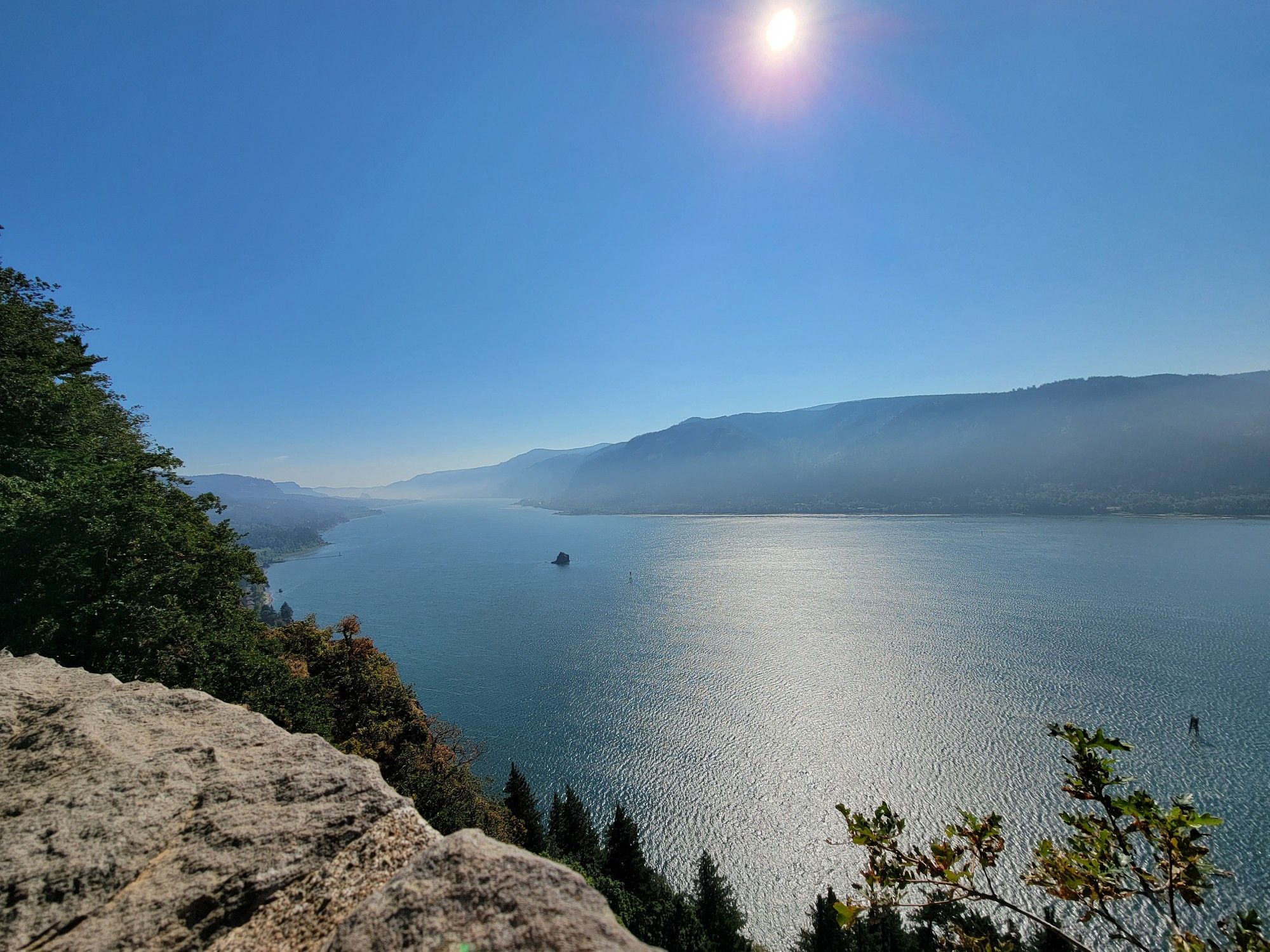 Sunny river vista from a rocky cliff, with distant mountains and bright sun. - Cape Horn Trail