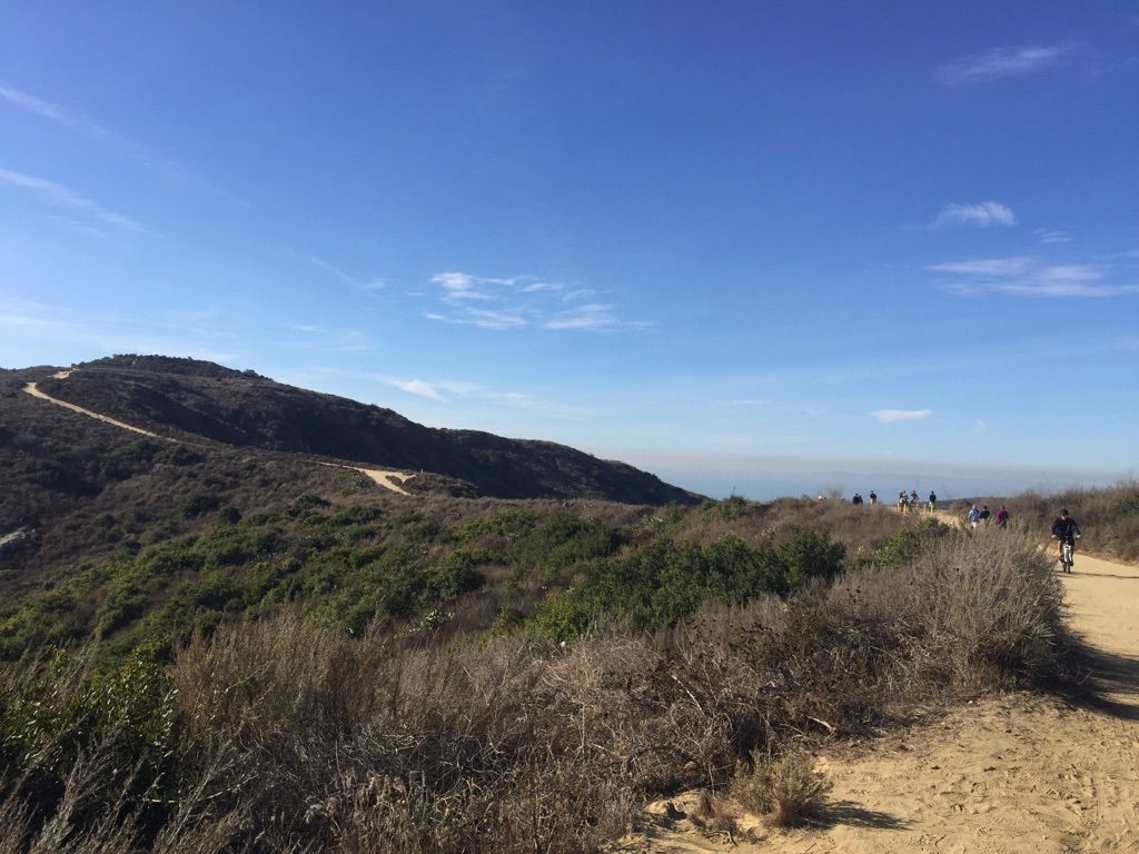People walk and bike on a dirt trail winding through brush-covered hills. - Wood Canyon and Rock-It Loop
