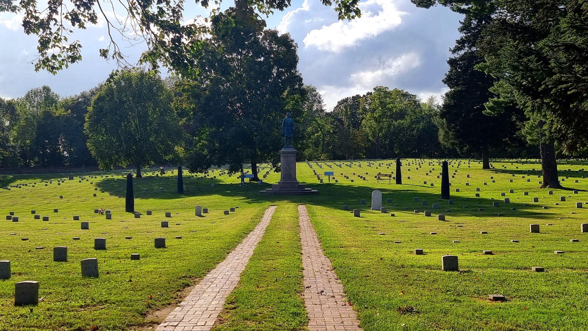 A brick path leads through a large cemetery with many small headstones. - Sunken Road Walking Trail