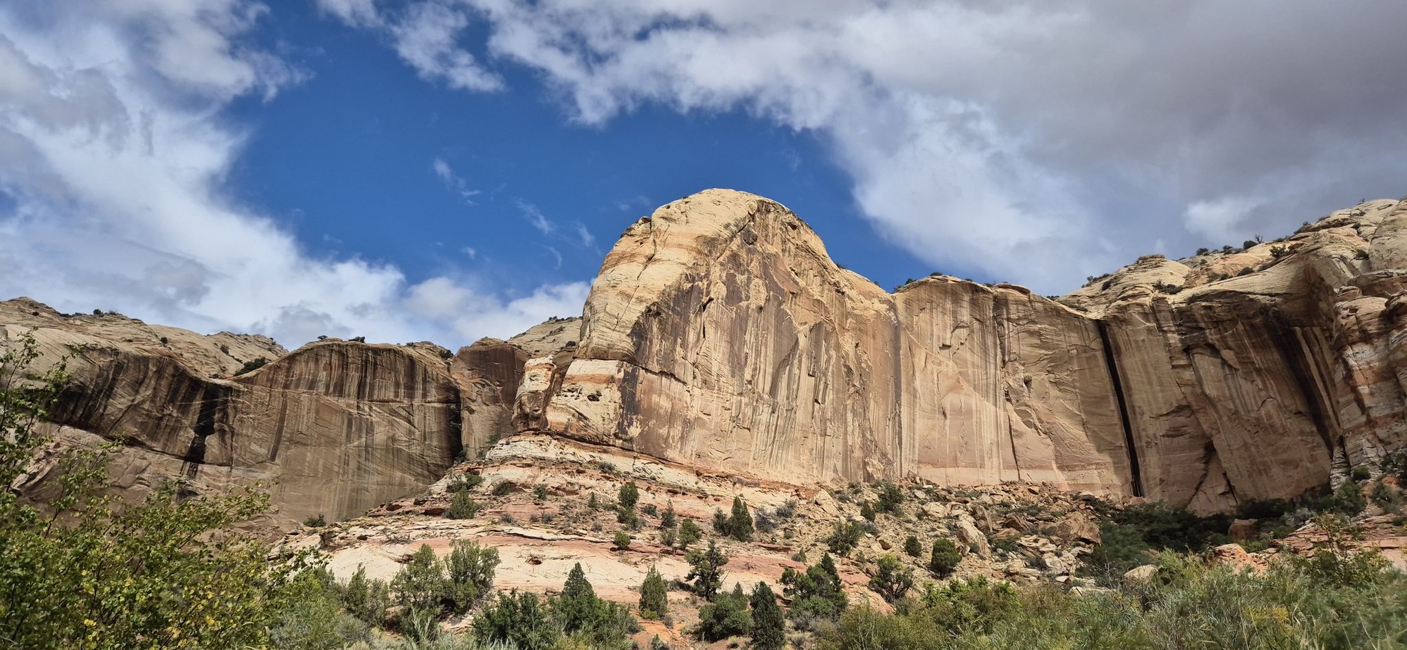 A large, textured rock formation stands against a blue and cloudy sky. - Lower Calf Creek Falls Trail