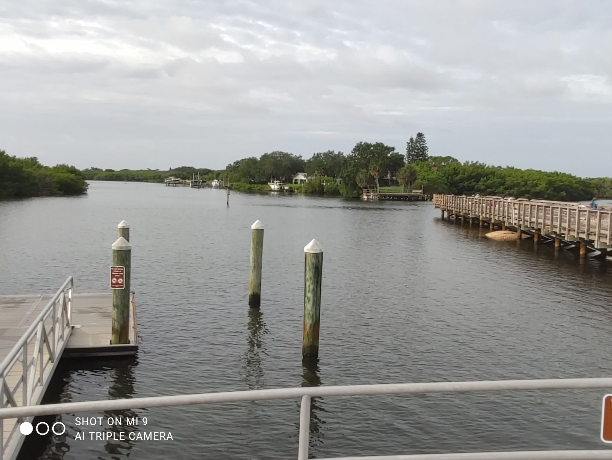 Overcast view of a calm waterway with docks and a long wooden bridge. - Friendship Trail and Ballast Point Loop
