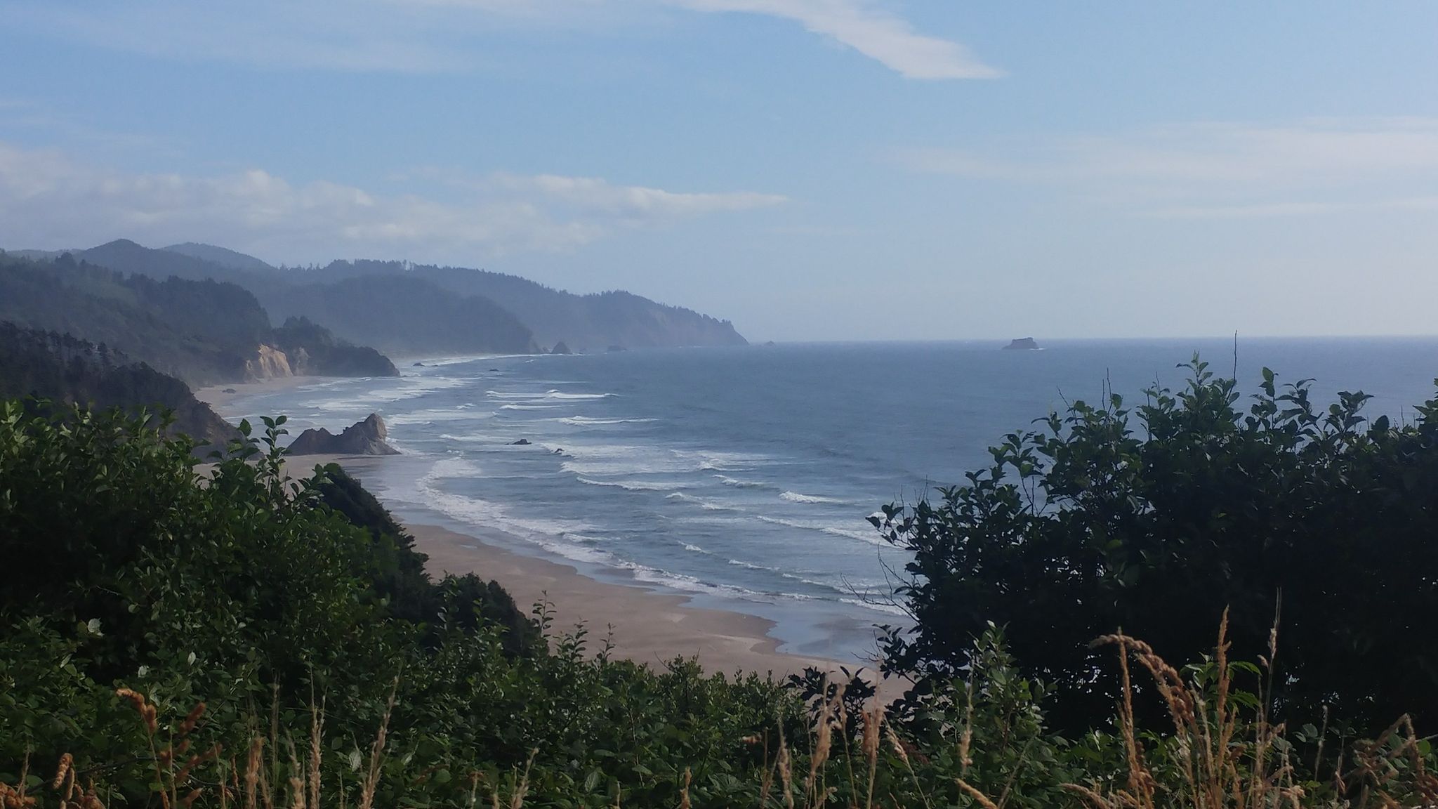 Clear day view of a rugged coastline, sandy beach, and ocean with waves. - Oregon Coast Scenic Bikeway