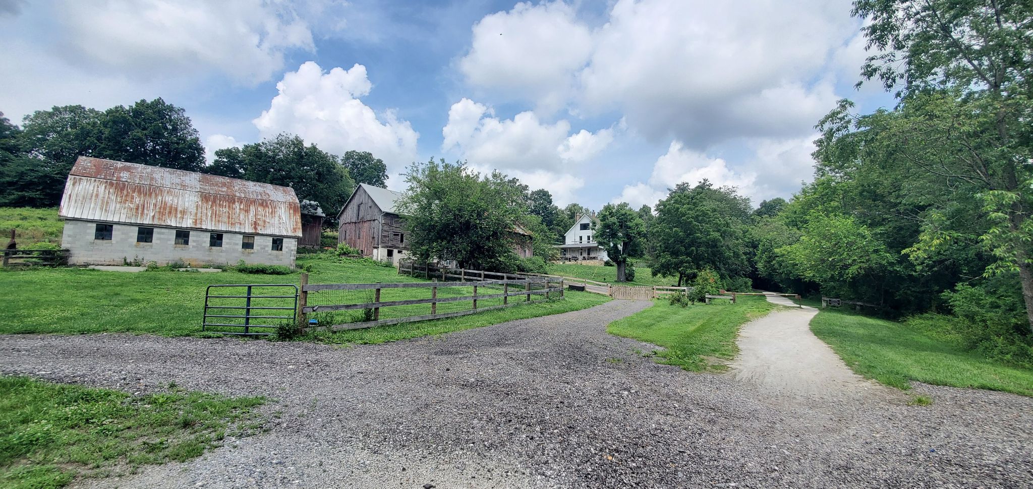 Old farm buildings and a gravel road fork under a cloudy sky. - Torrey C. Brown Rail Trail