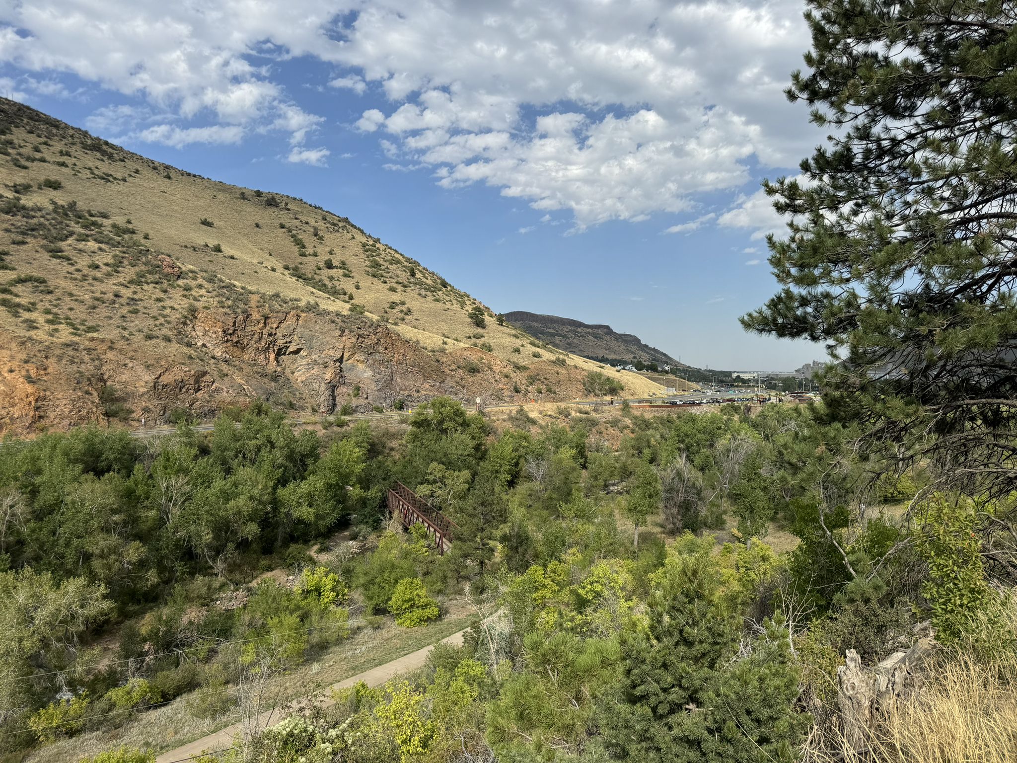 Mountain landscape with a river, green trees, and a distant bridge under a cloudy sky. - Peaks to Plains and Welch Ditch Loop