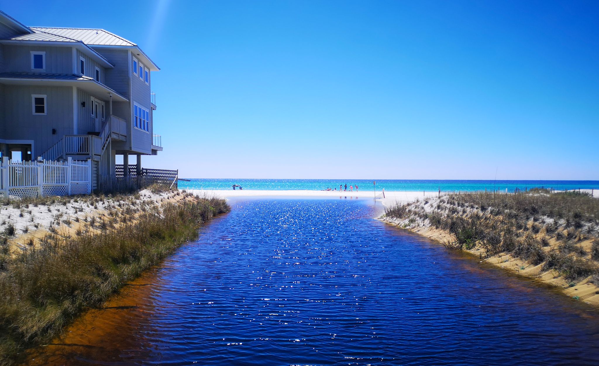 A stream flows to a bright blue ocean beach, with a house nearby. - Bench With Lake View – Private Beach loop from Jolee Island