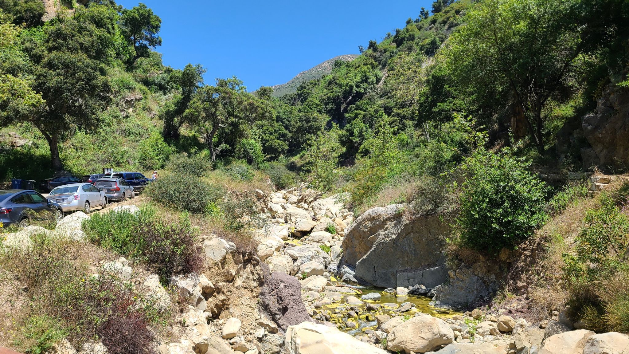 Dry, rocky riverbed with cars parked on the bank under a clear sky. - Hot Springs and Cold Spring Trail Loop
