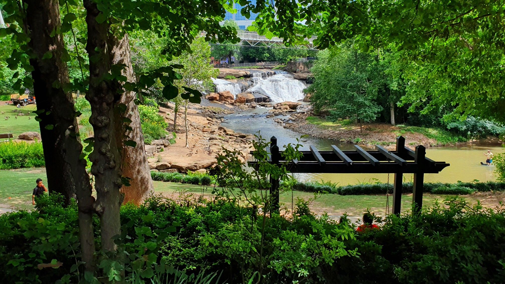Lush green park with a waterfall, river, and people enjoying the outdoors. - Cleveland Park – Vietnam Veterans Memorial loop from Lot E