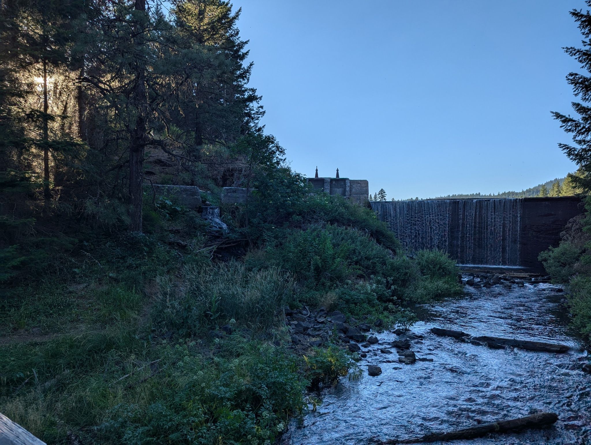 River flowing from a dam through a forest, with sun peeking through trees. - Keene Creek Dam – PCT Trail Access loop from Green Springs Summit Trailhead