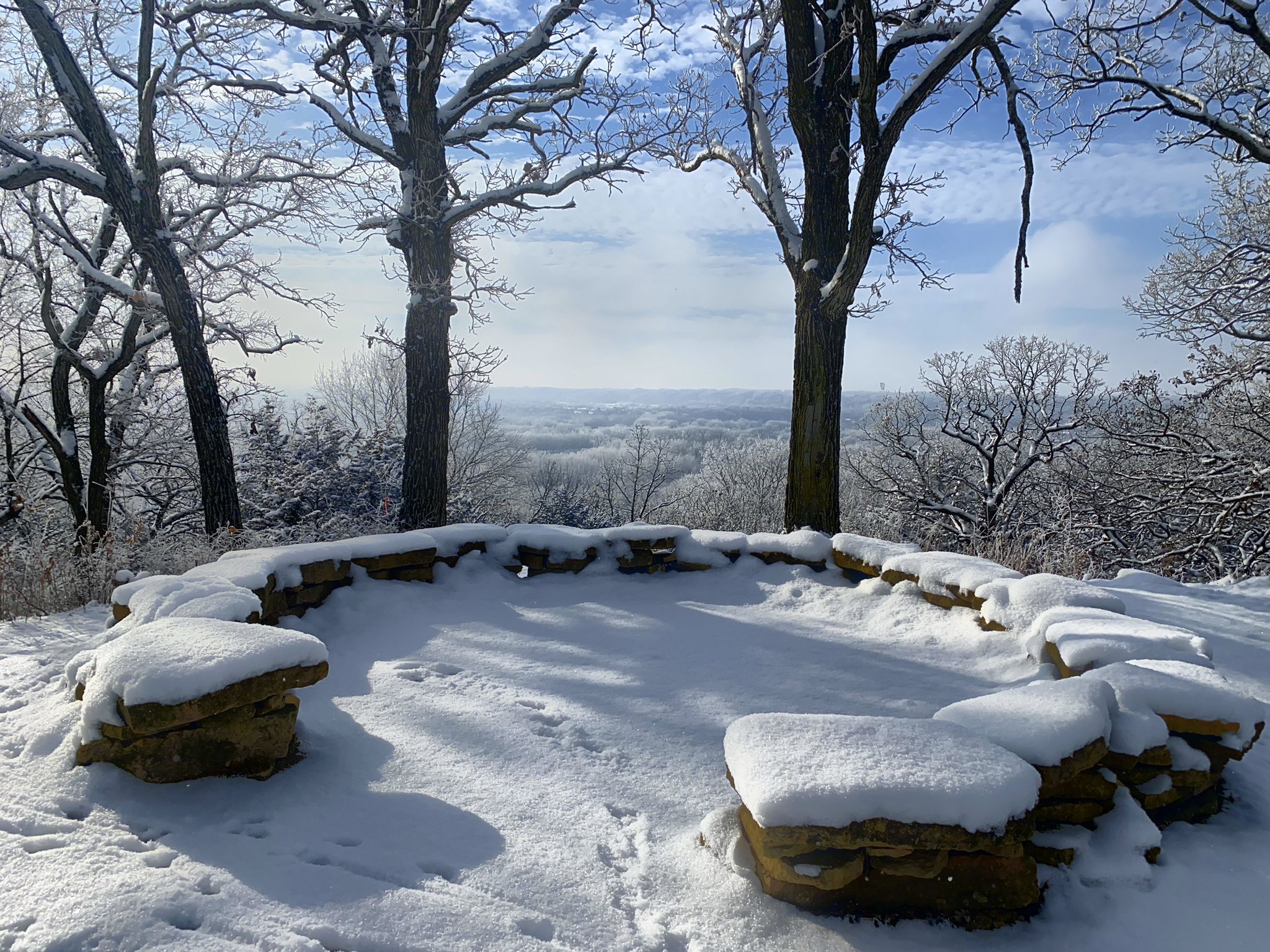 Snowy stone seating area overlooking a winter forest valley on a bright day. - Stagecoach, Ravine, Field, and Pond Loop