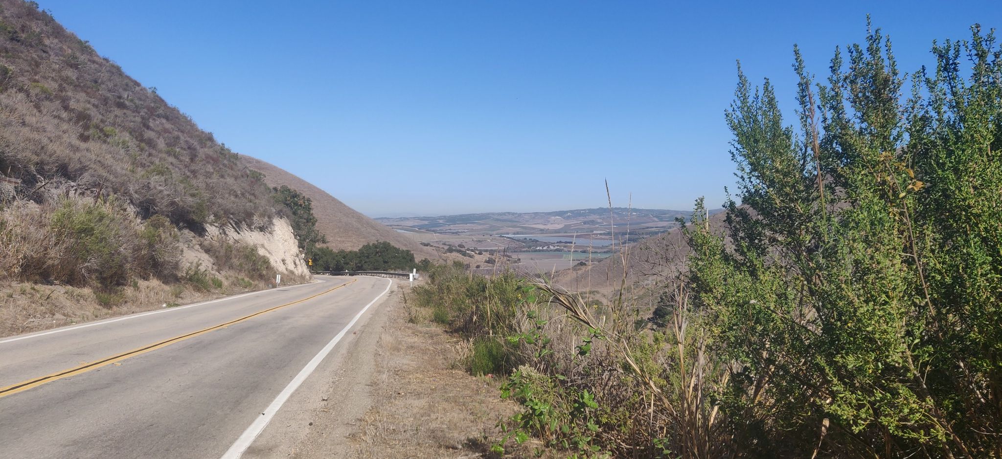 A winding road alongside a dry hillside under a clear blue sky. - Drum Canyon Road loop from Los Alamos