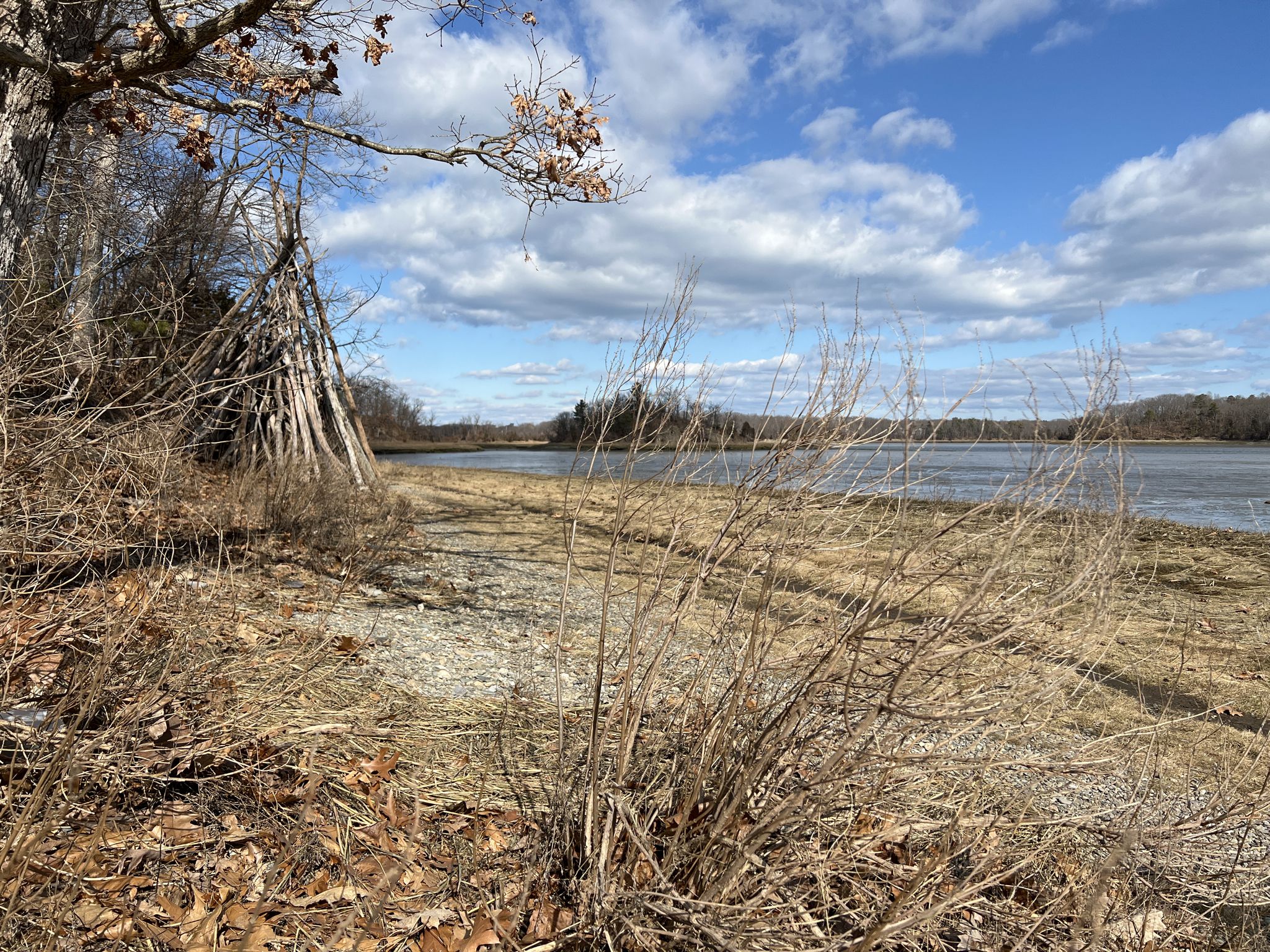 A teepee-like structure by a wide river, with dry grass and cloudy sky. - Weymouth Back River Walk & Osprey Overlook Park loop