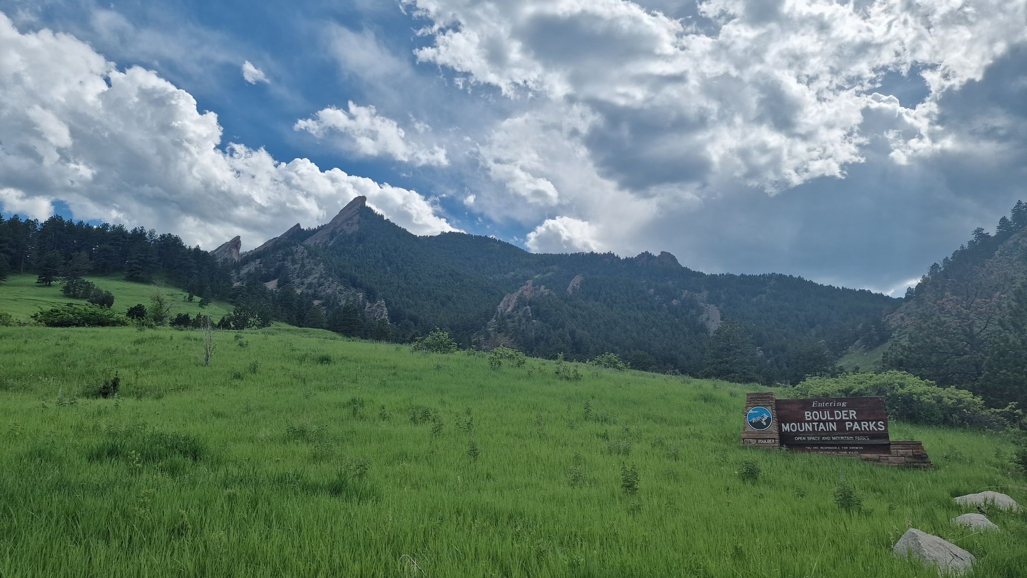 A vast green field with dramatic mountains under a cloudy sky. - Flagstaff Road Scenic Drive – Gross Reservoir loop from Culinary School of the Rockies