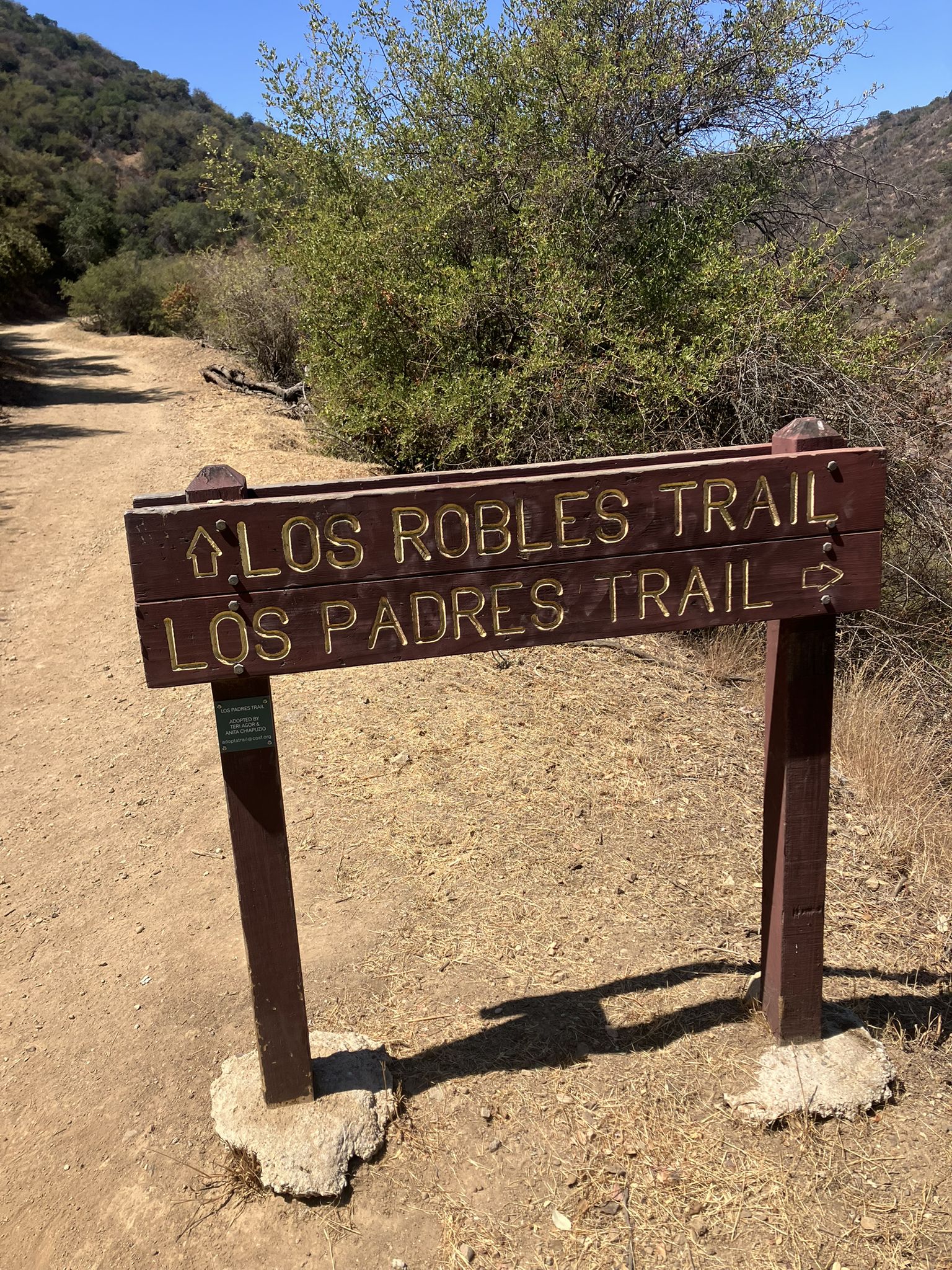 A wooden trail marker stands on a sunny dirt path in a hilly landscape. - Los Padres Open Space loop from American Eagle Outfitters