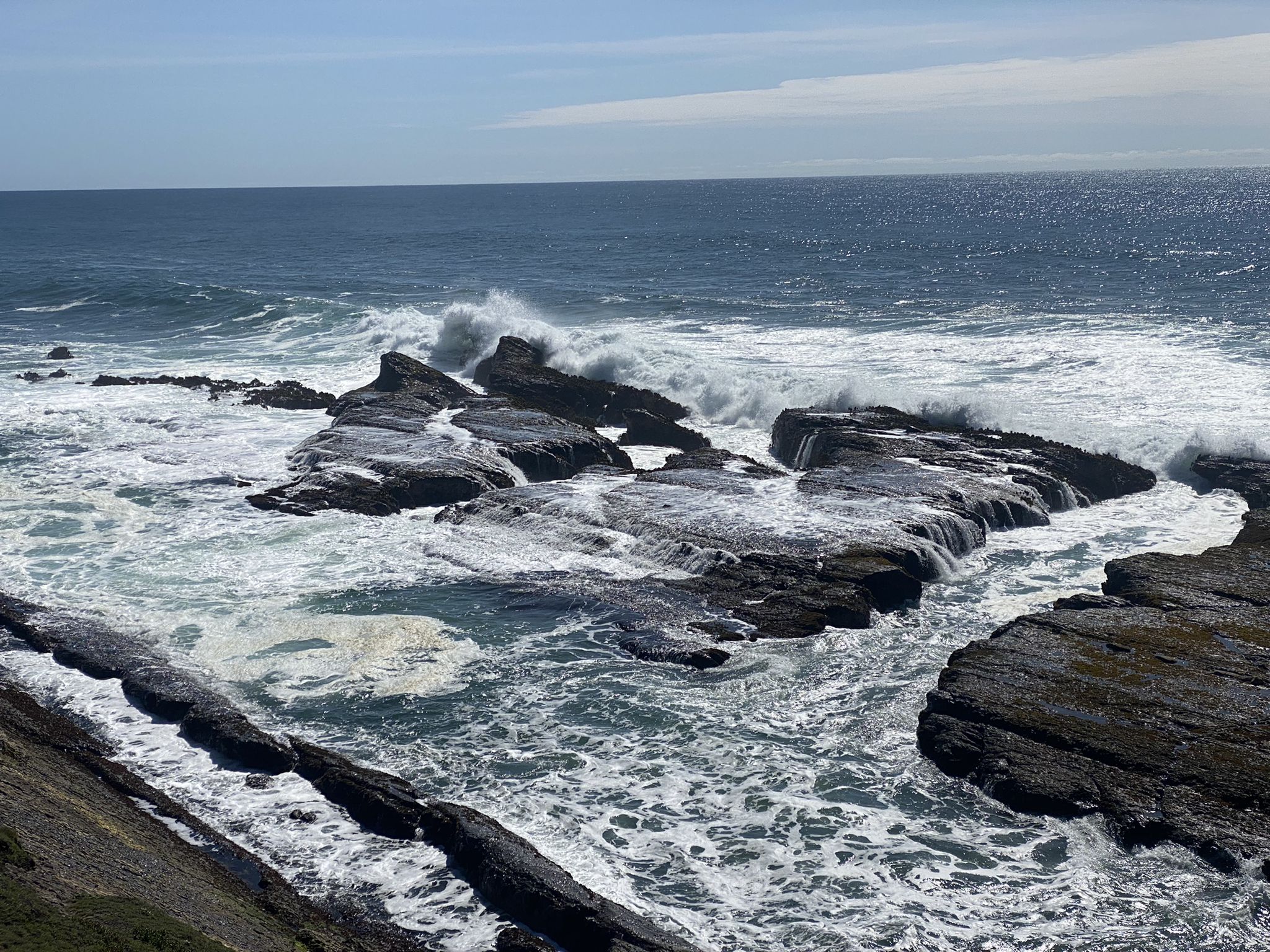 Ocean waves crash dramatically against dark, layered coastal rocks under a bright sky. - Point Arena-Stornetta Unit of the California Coastal National Monument