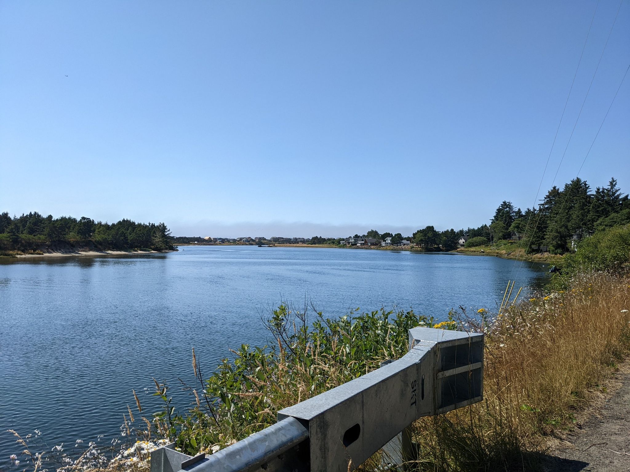 Wide river with forested banks and distant buildings under a clear sky. - Tillamook & Pacific City loop via Oregon Coast Scenic Bikeway