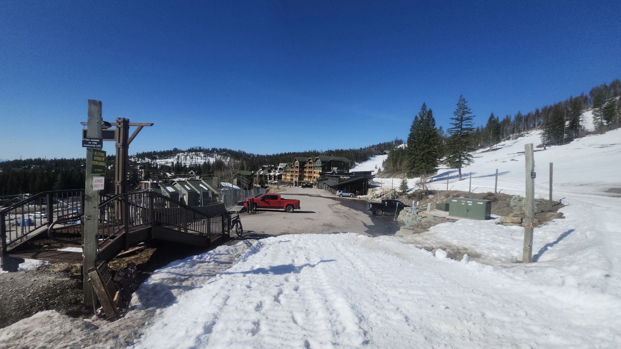 Snowy resort area with buildings, a red truck, and a wooden bridge. - Summit Trail