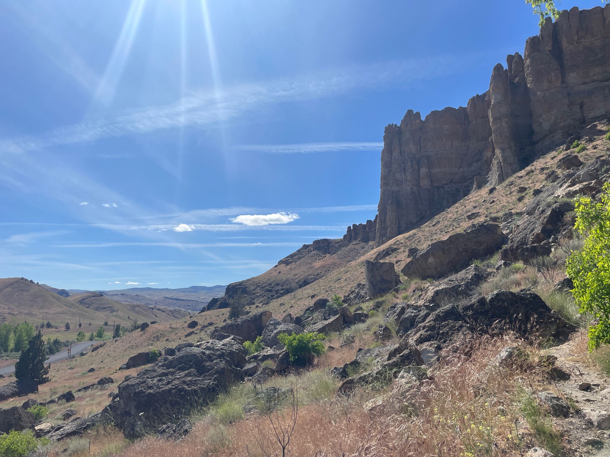 A long, jagged rock wall overlooks a dry valley under a bright, sunny sky. - Trail of the Fossils – Clarno Arch loop from Fossil