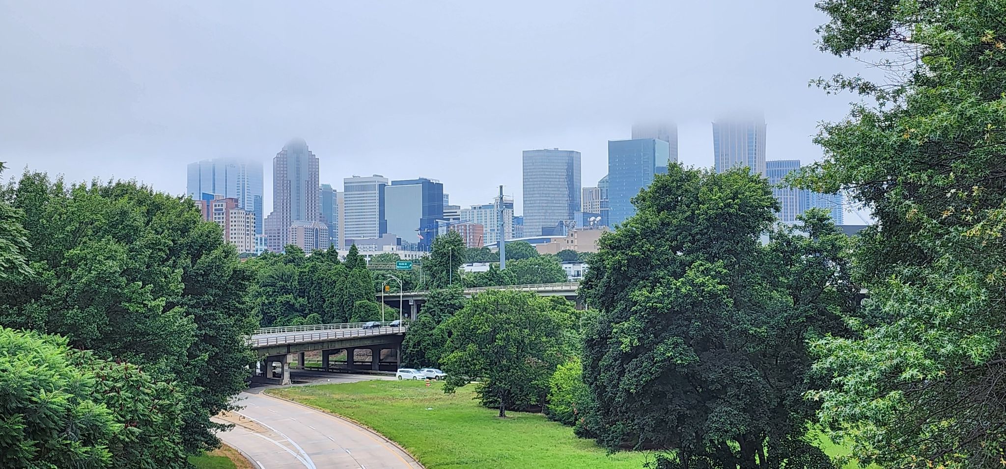 Overcast city skyline with tall buildings, green trees, and a road bridge. - Charlotte to Reedy Creek Nature Preserve loop