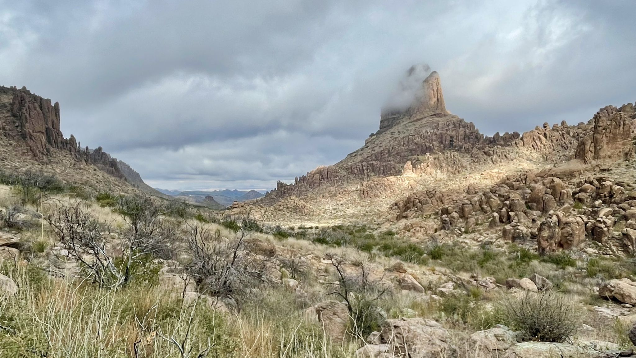 Desert valley with rocky mountains under cloudy sky, prominent peak with cloud. - Weavers Needle Loop Trail