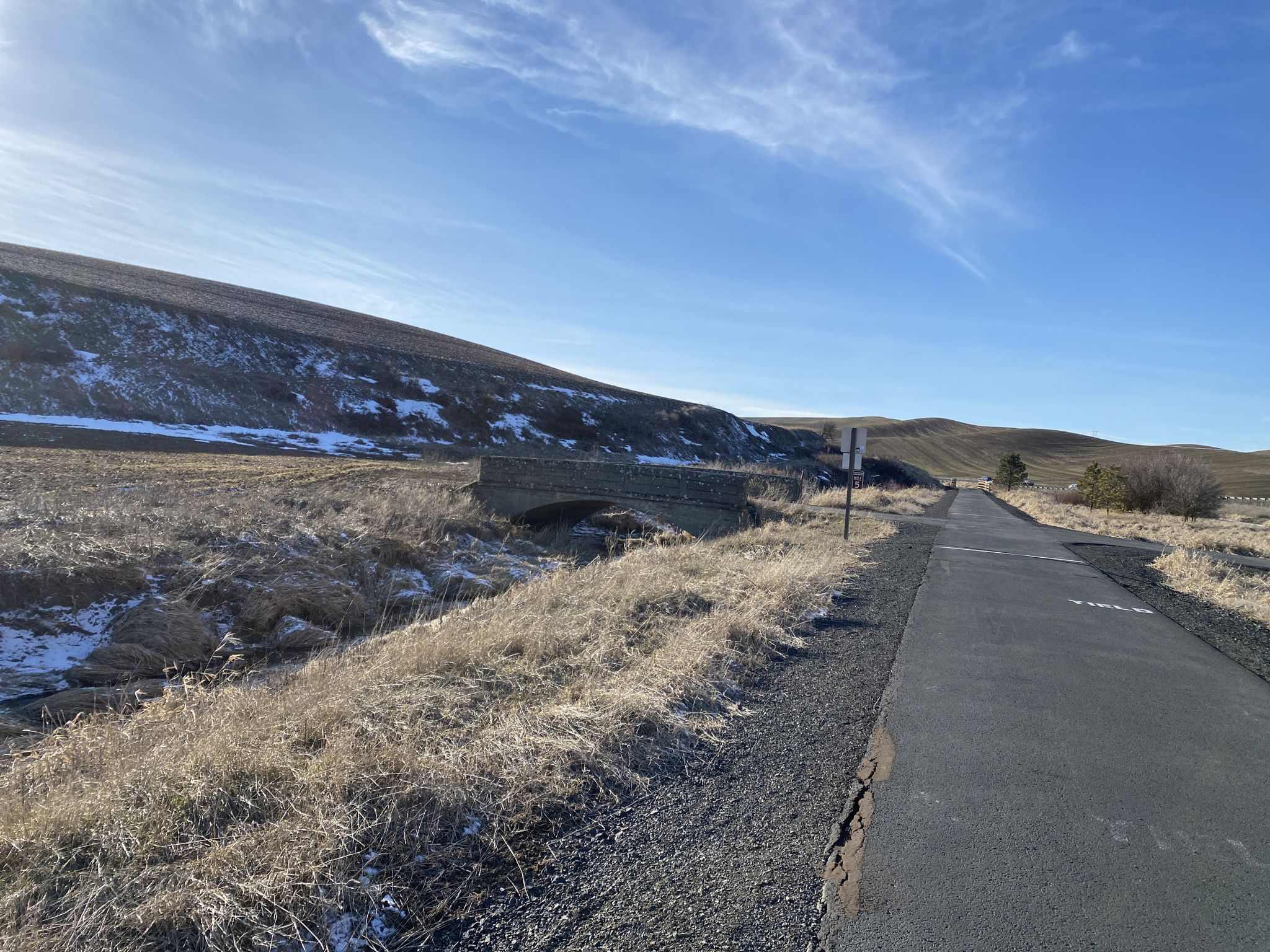 Paved path alongside dry grassy hills with a stone bridge under a bright sky. - Sunshine Road underpass loop from Moscow