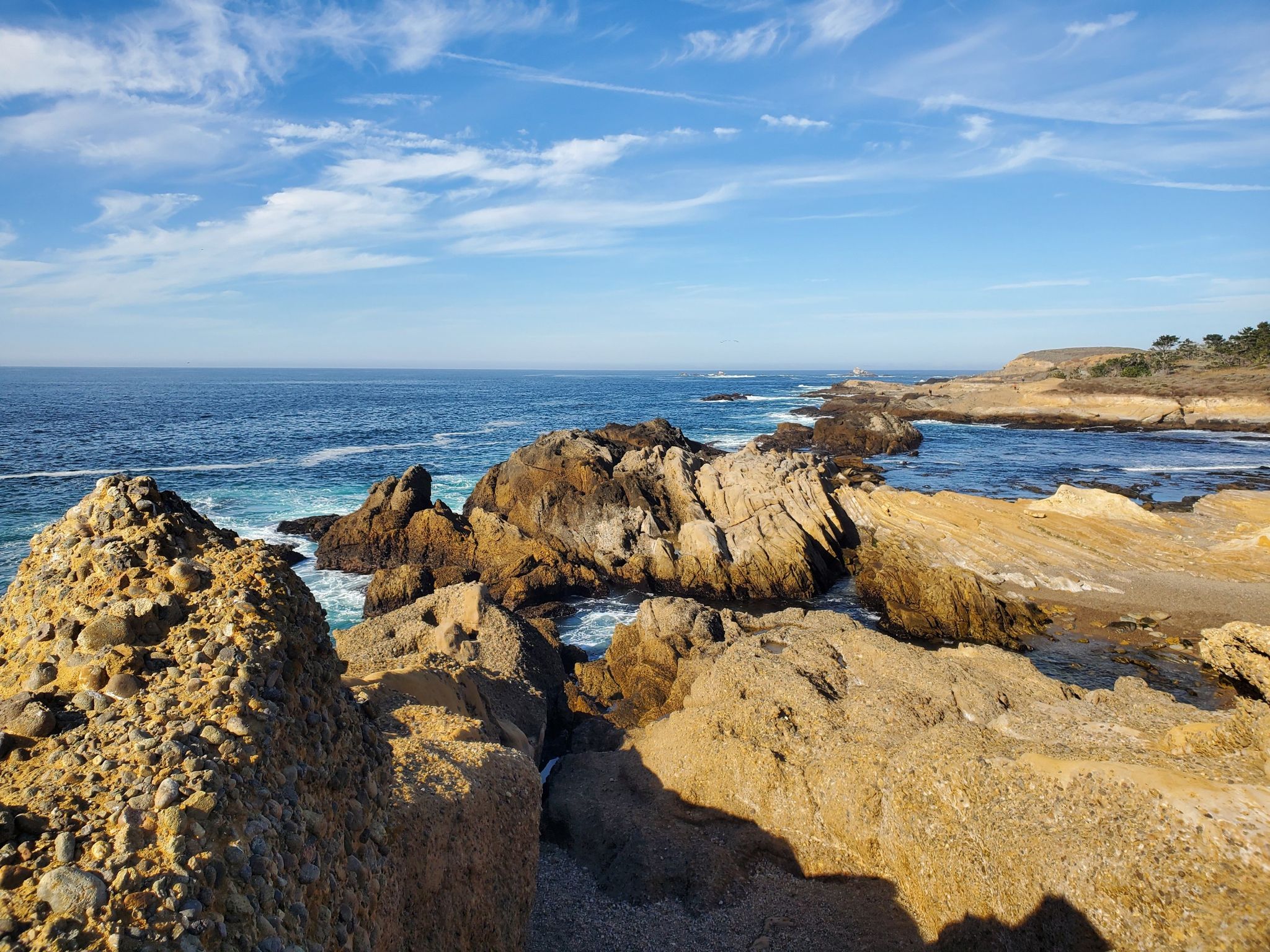 Rocky coastline with ocean waves under a bright blue sky with wispy clouds. - Point Lobos loop from Whaler's Cove
