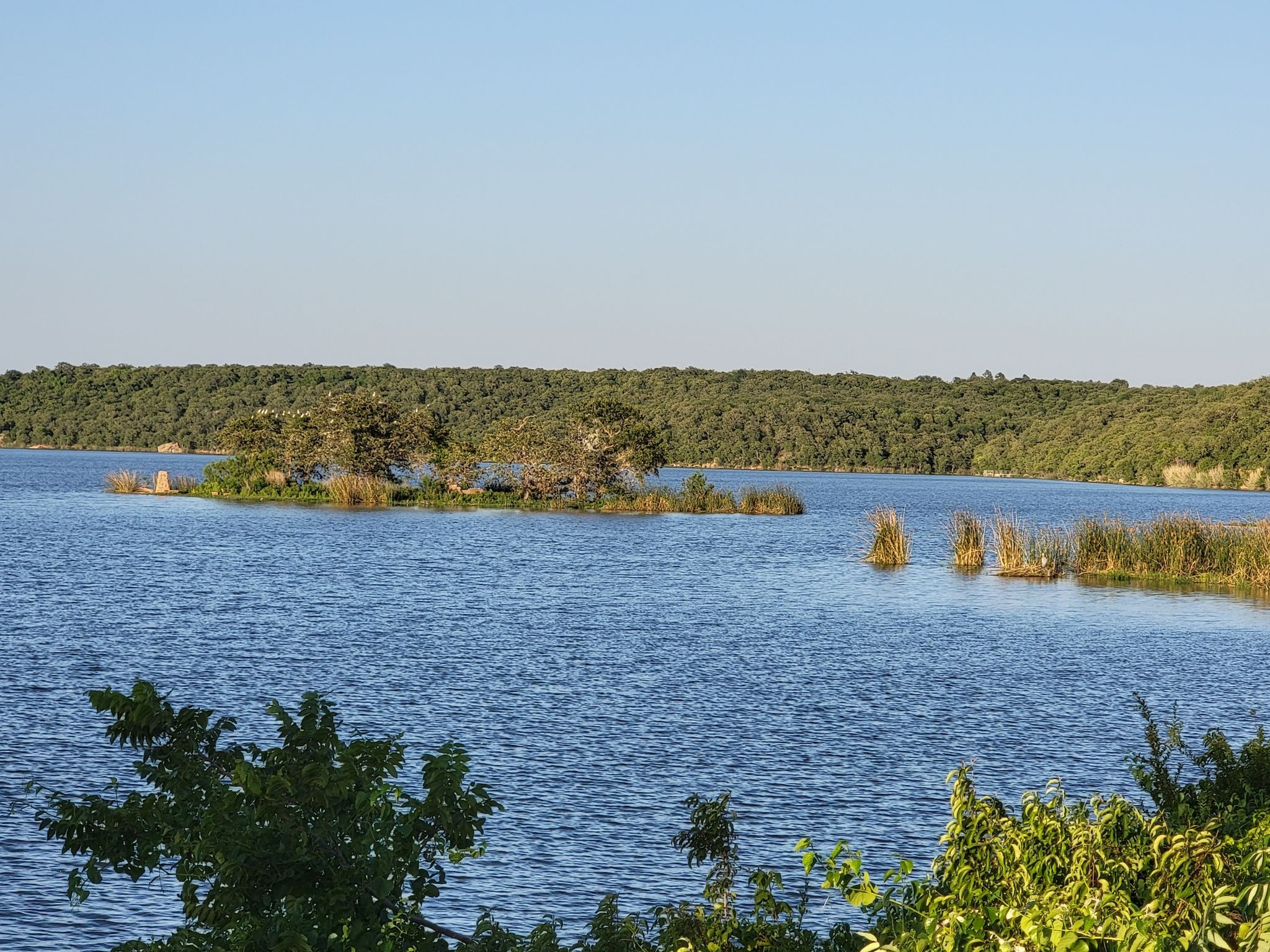 Sunny lake with small tree-covered islands and distant green shoreline. - Cross Timbers Trail Loop