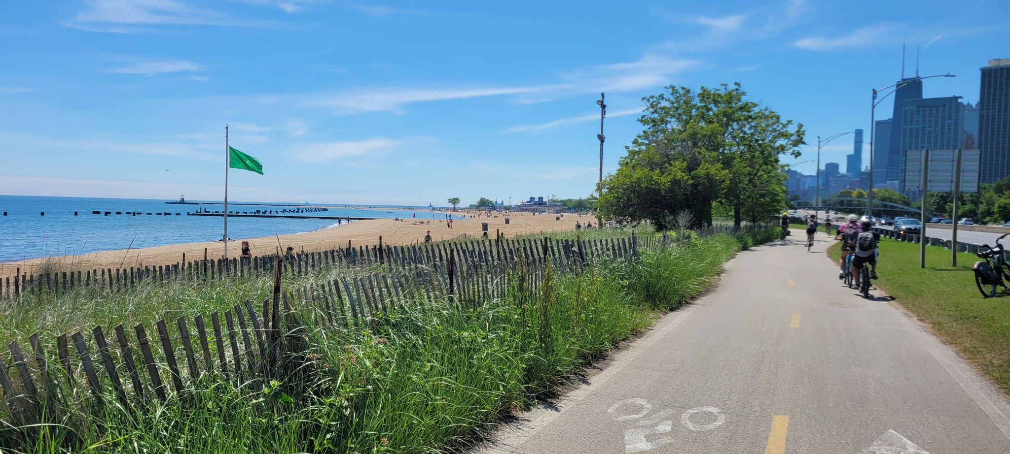 Cyclists on a paved path next to a sandy beach and calm water. - Lincoln Park – Lakefront Trail, Chicago loop from Dempster-Skokie