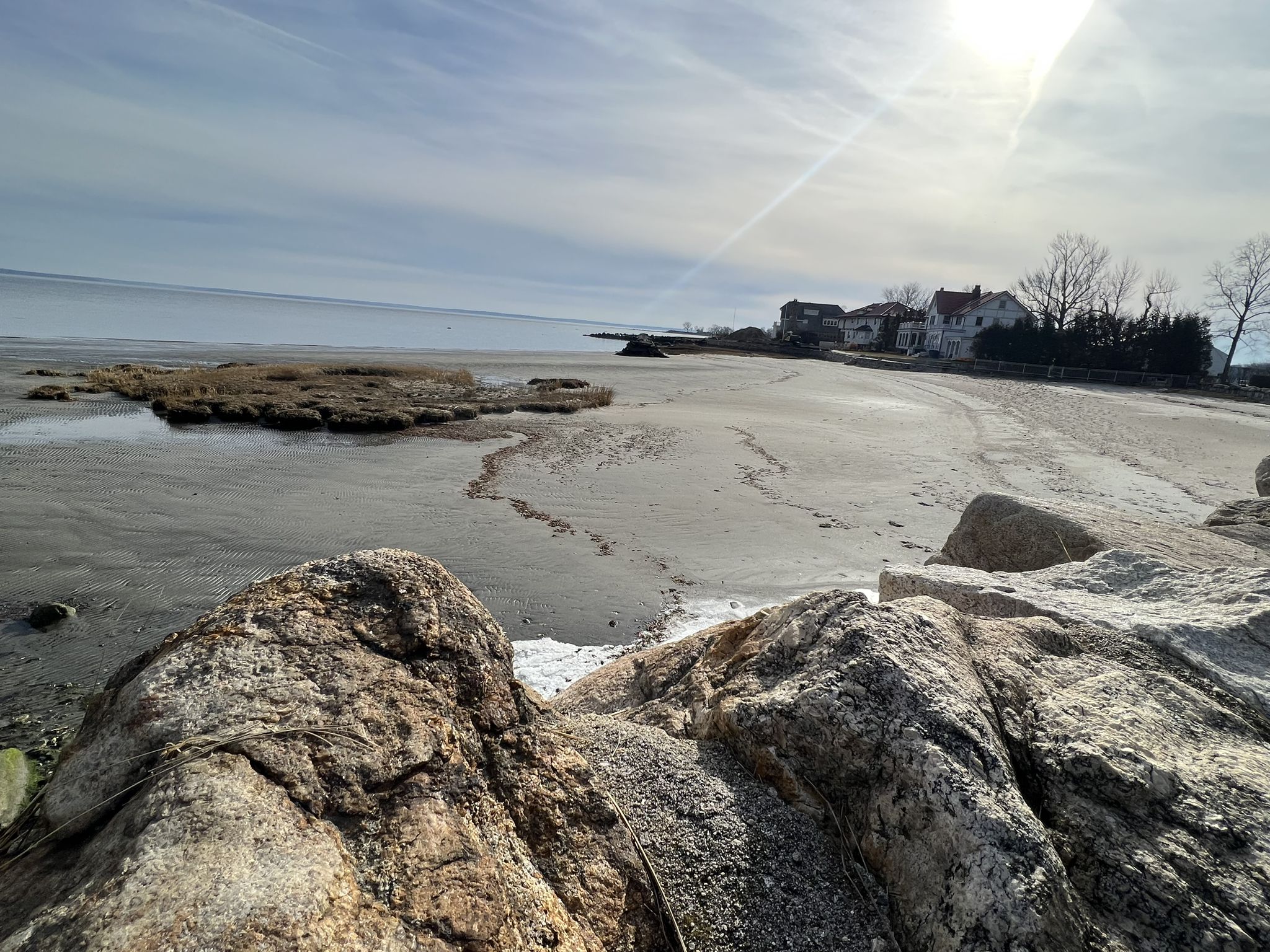 Sunny sandy beach with large rocks, distant houses, and bright sky. - Greenwich Point Park loop