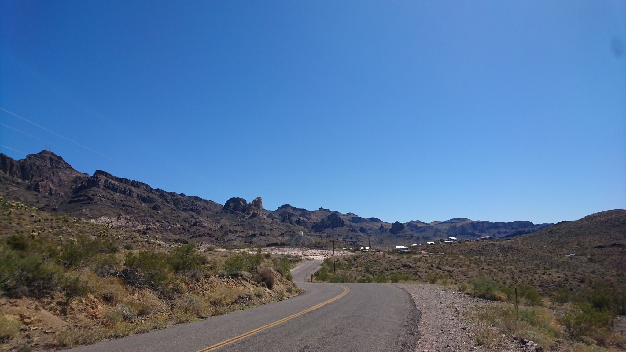 A winding desert road leads towards distant mountains under a clear blue sky. - Bullhead City to Oatman via Silver Creek Road