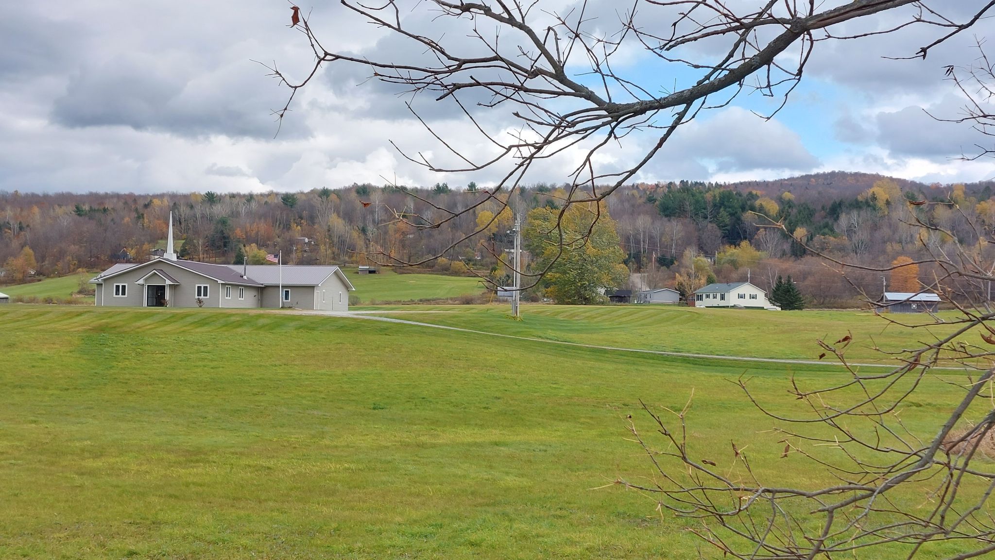 Building with a steeple in a green field, surrounded by autumn hills under clouds. - Big Falls Waterfall – Jay Peak Pass loop from Big Falls State Park
