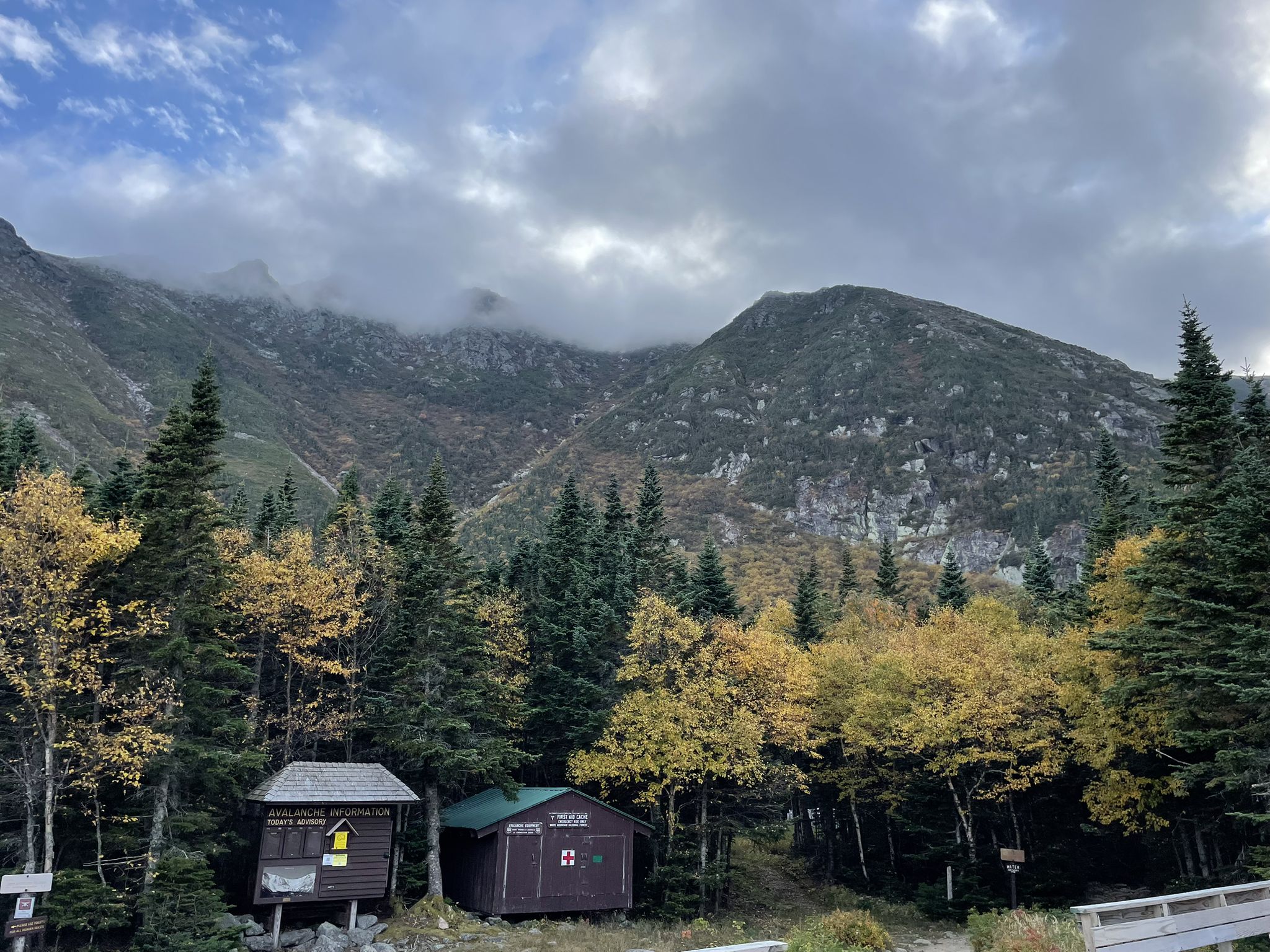 Two small cabins nestled among autumn trees at a cloudy mountain base. - Boott Spur and Tuckerman Ravine Loop