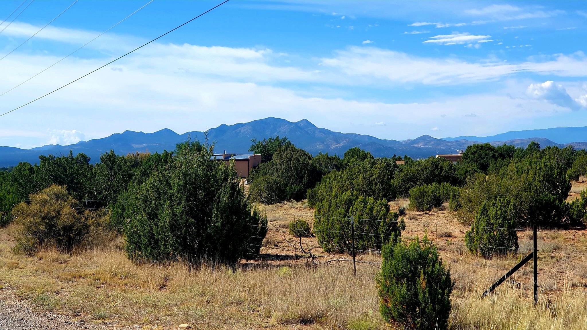 Arid landscape with scattered green trees and distant mountains under a bright blue sky. - South Santa Fe half century