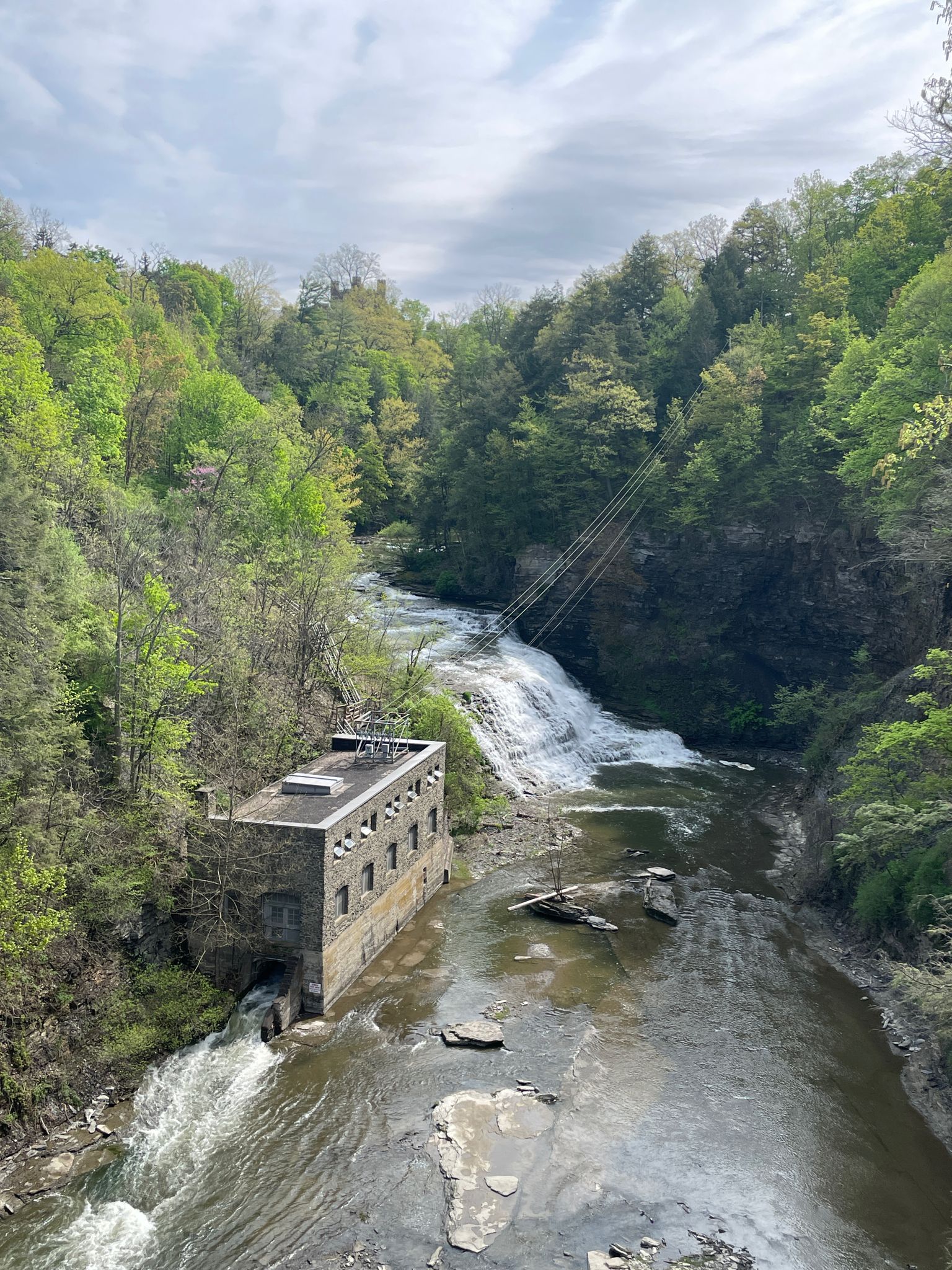 A stone building sits in a river with a waterfall and lush green gorge. - Fall Creek Forest Horseshoe Falls