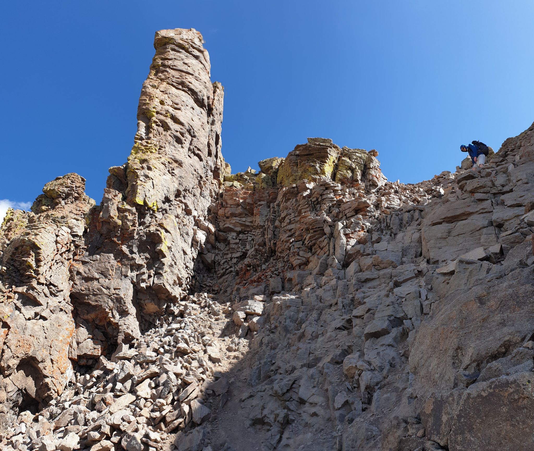 Person climbing a steep, rocky mountain slope with a tall rock spire. - Wetterhorn Peak and Uncompahgre Peak