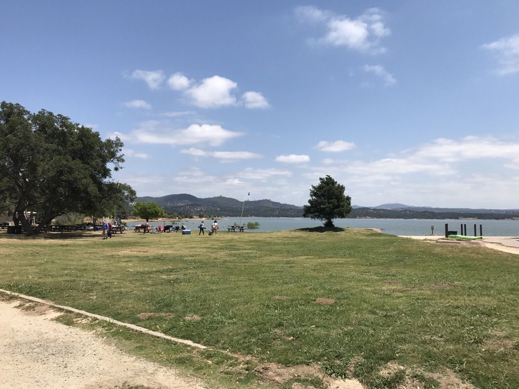 People gather on a grassy field beside a large lake and distant hills. - Granite Bay loop from Miners Ravine Nature Reserve