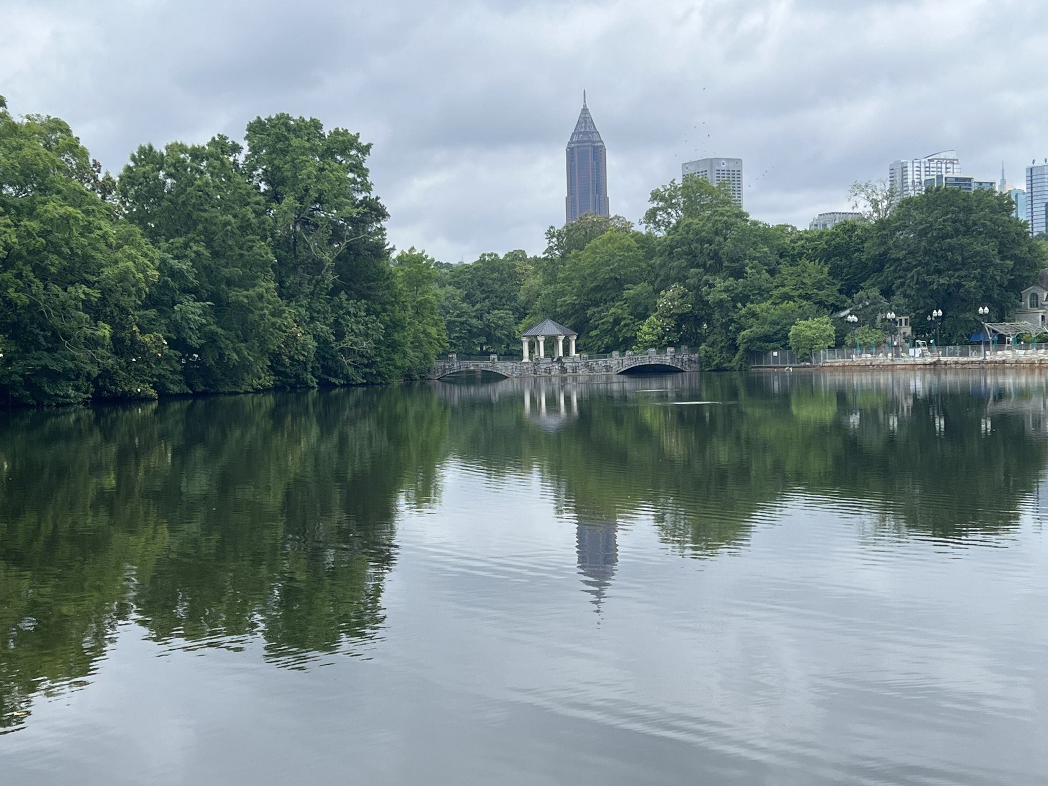 Lake reflecting a bridge and distant city buildings under an overcast sky. - Atlanta Beltline Trail