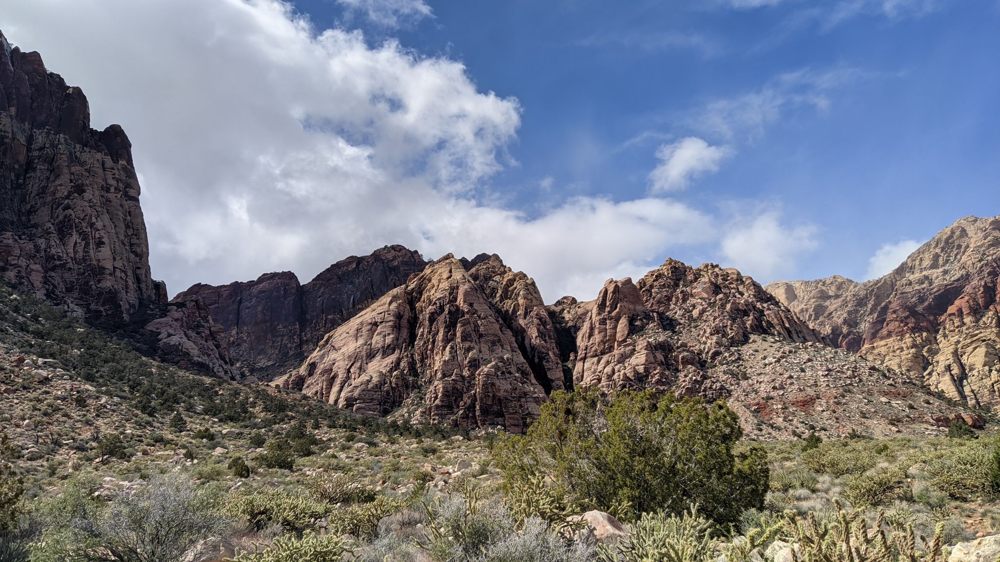 Towering red rock mountains and desert vegetation under a bright, partly cloudy sky. - Middle Oak Creek Trail – Pine Creek loop from Red Rock Canyon - Basin Trail Dirt Parking Lot