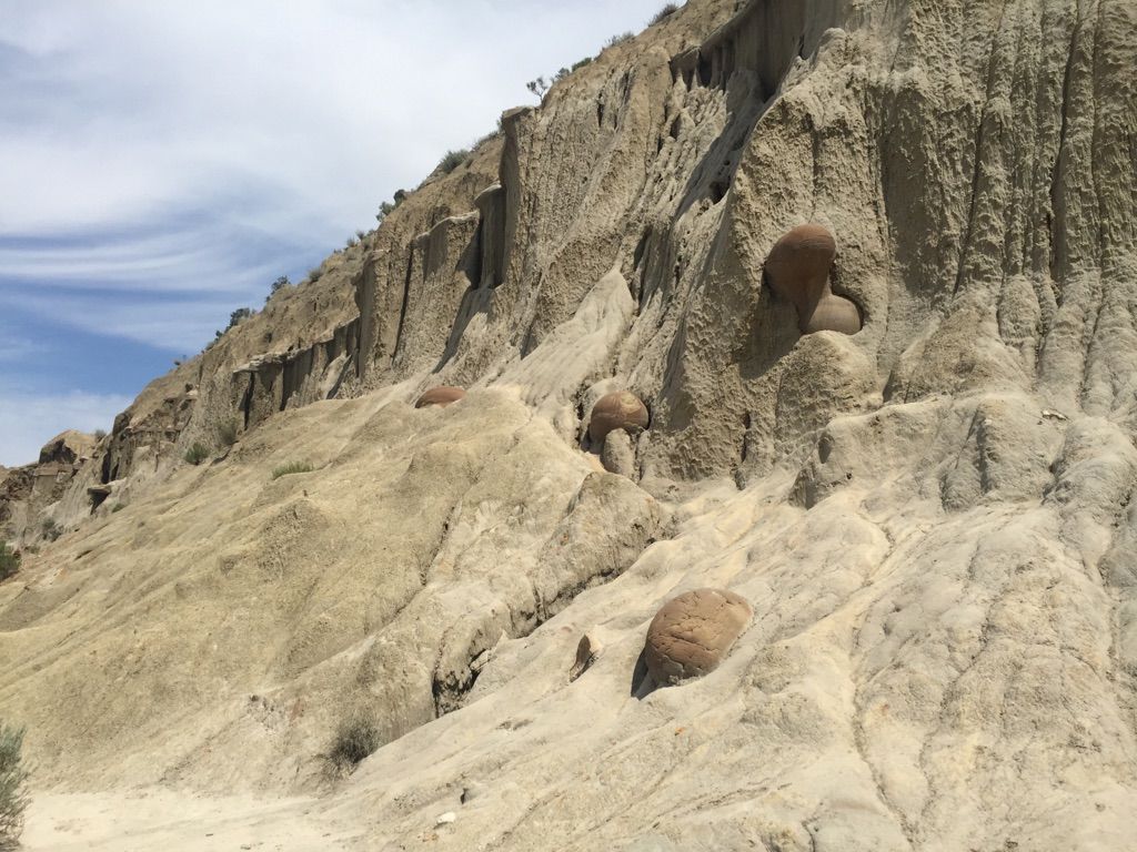 Badlands landscape with a steep, eroded cliff face and large spherical rock formations. - Buckhorn Trail